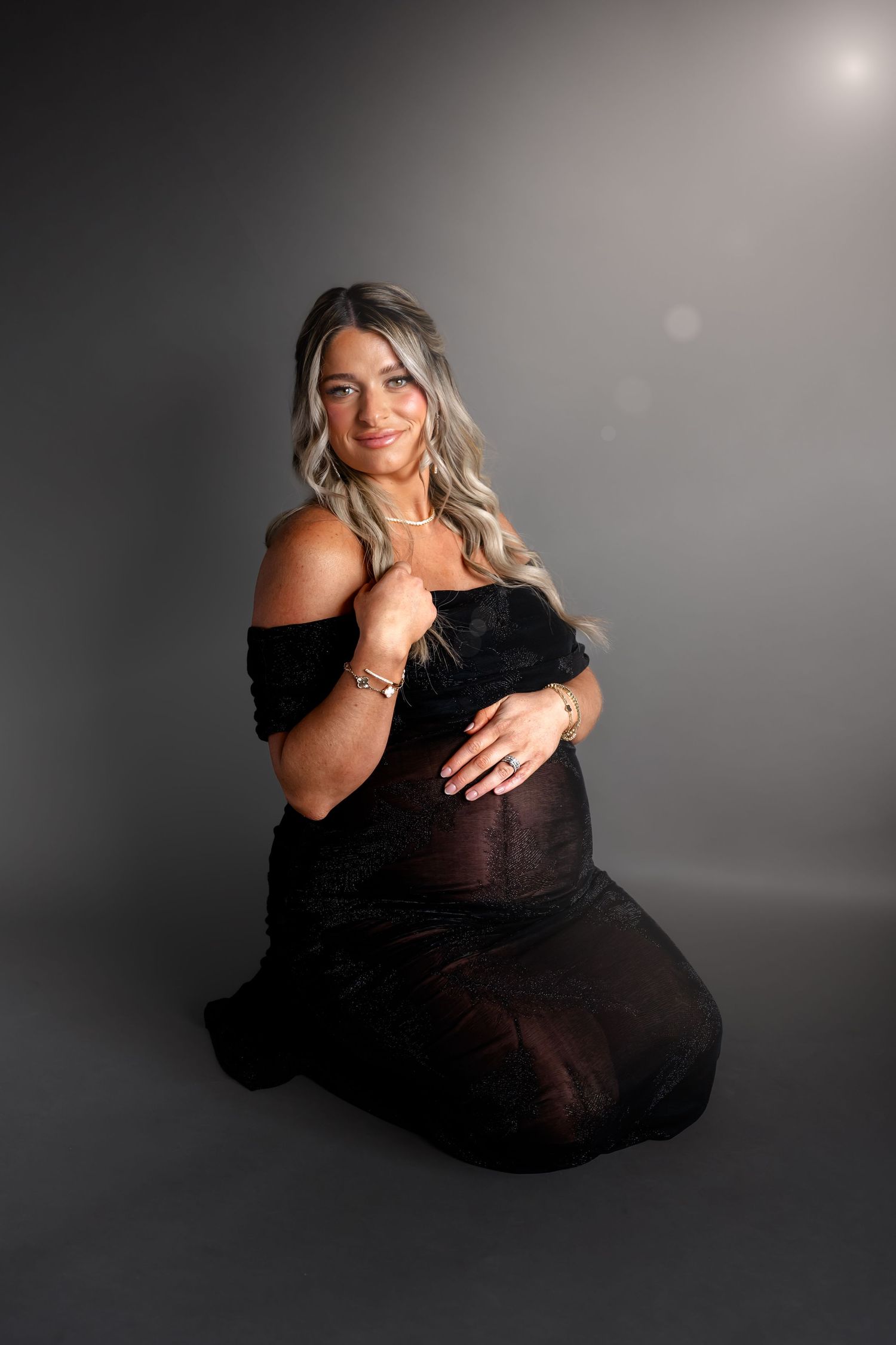 Elegant maternity photo with woman in black dress against dark background.