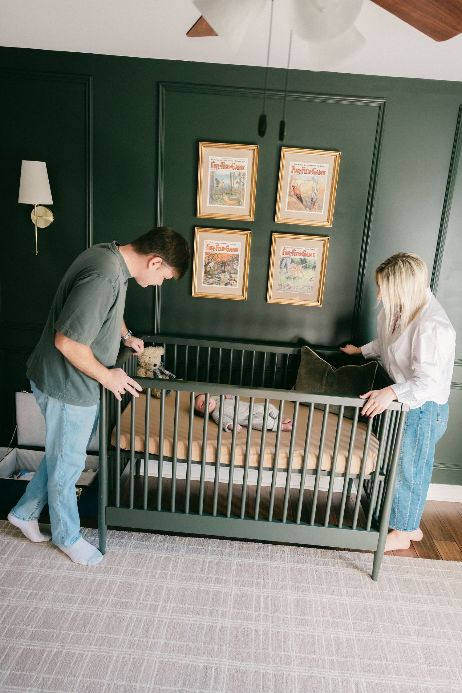 Two people assembling a dark wooden crib in a room with green walls.