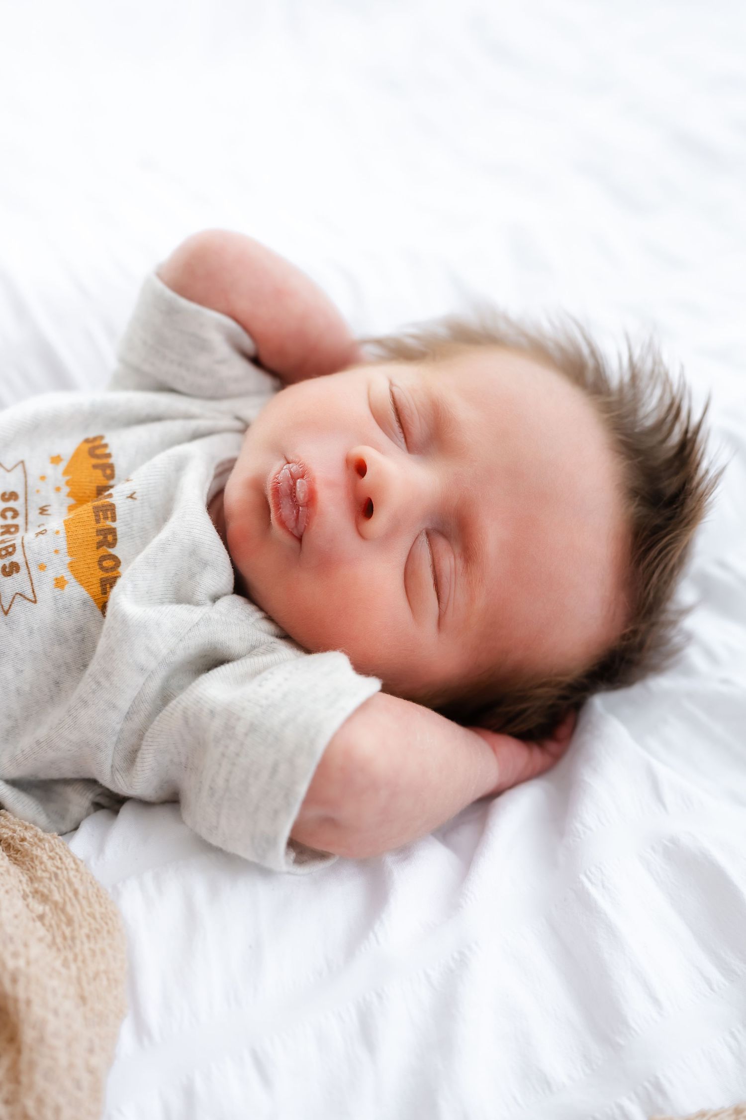 Sleeping baby in gray onesie rests peacefully on white bedding in a series of gentle poses.
