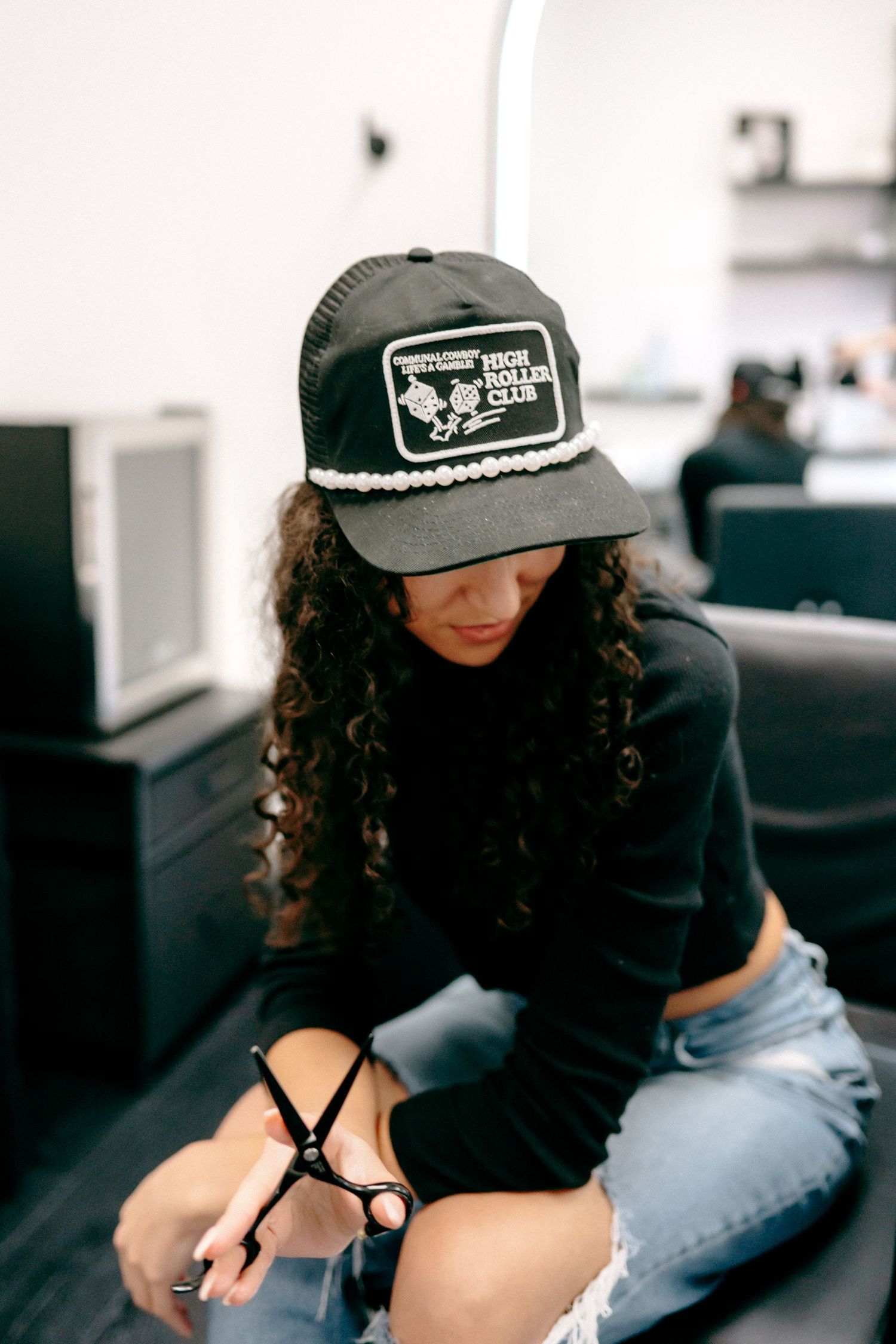 Person wearing a baseball cap and distressed jeans relaxes on dark furniture.