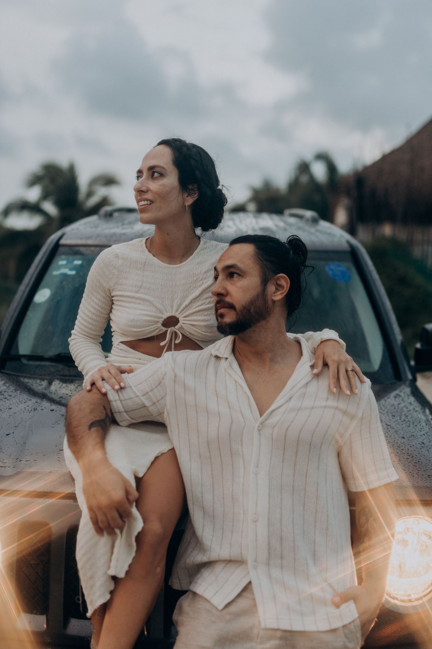 Romantic couple in light-colored outfits poses against a car during a photo session in Cancún, Mexico.