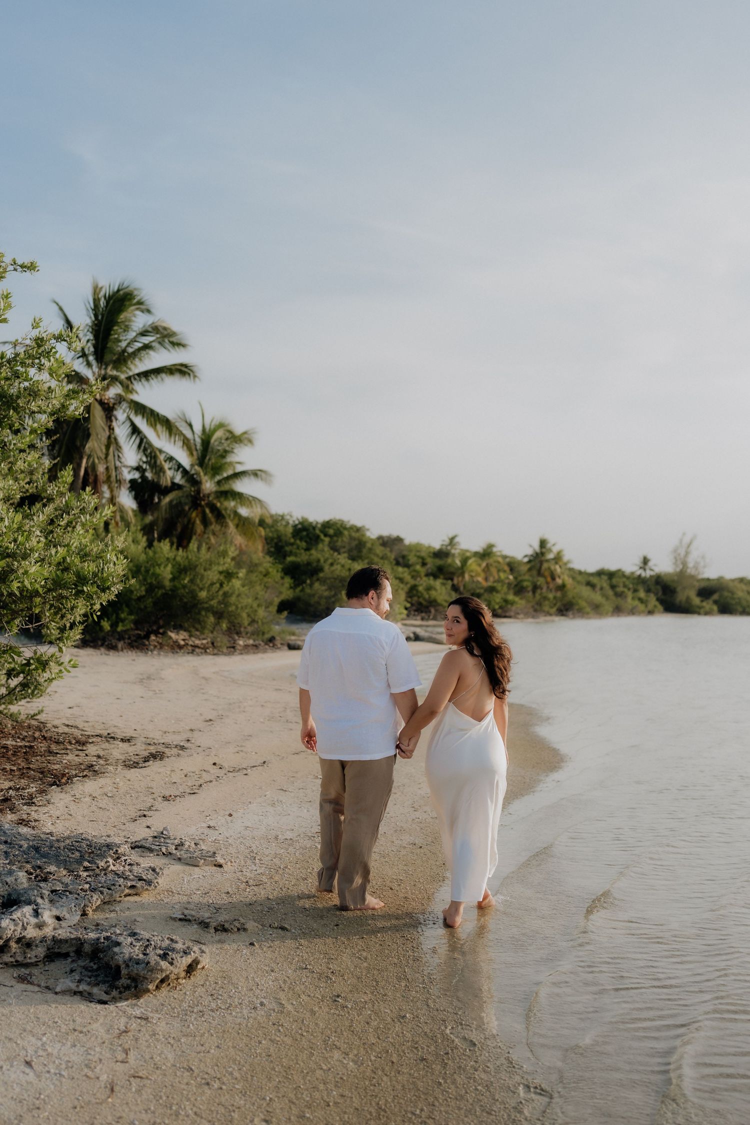 Couple holding hands walking along a tropical Tulum beach shoreline during a romantic save the date photoshoot