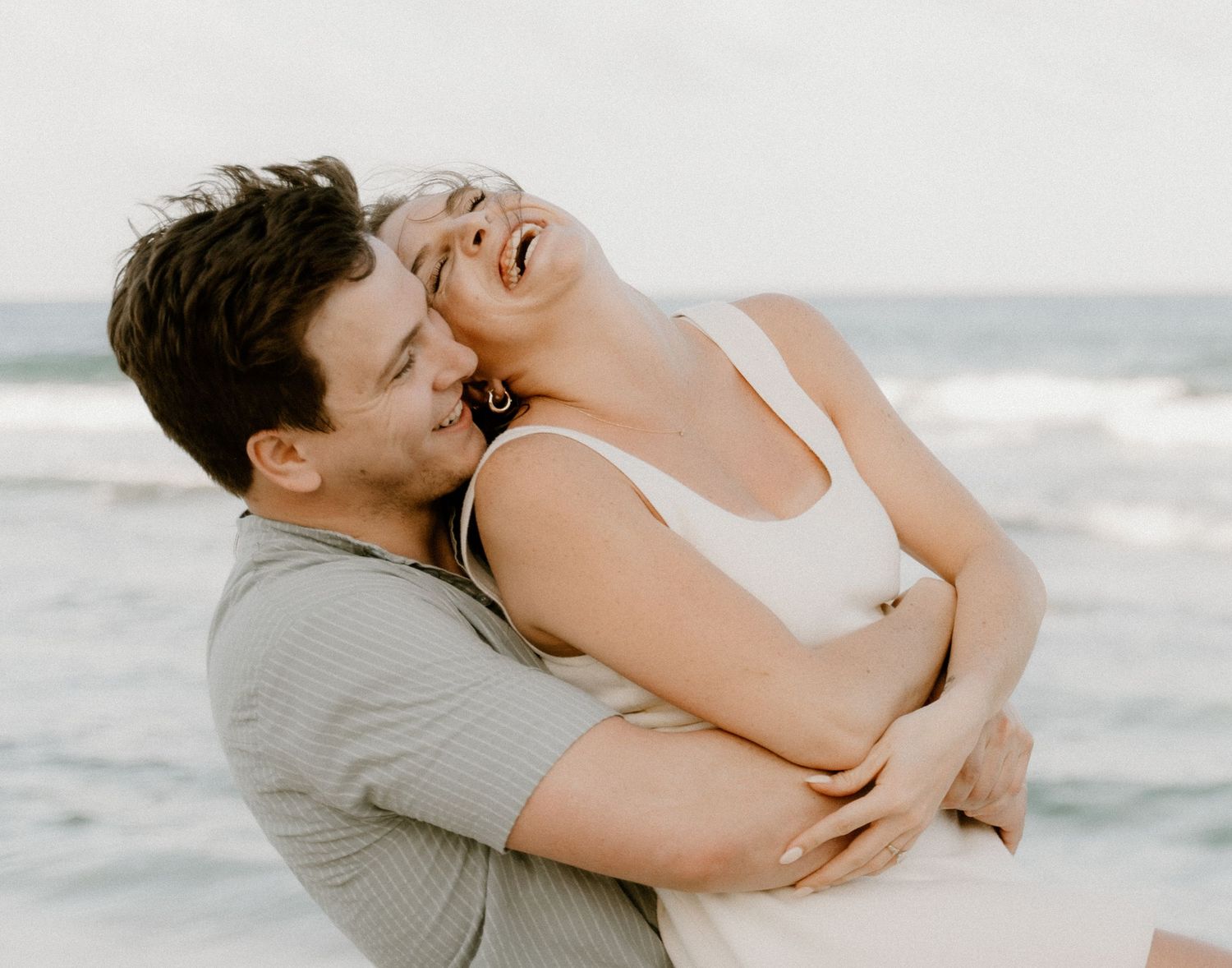Candid portrait of couple laughing and embracing on a beach in Isla Mujeres.