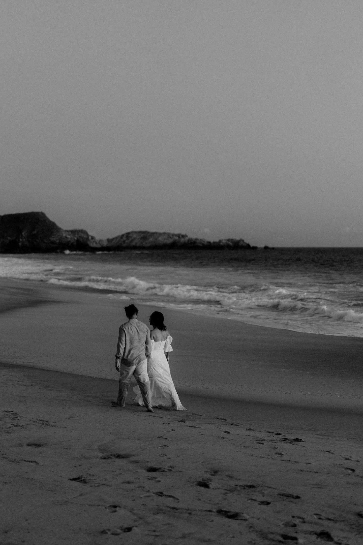 A couple walks together along a scenic beach shoreline in black and white in Mazunte, Mexico