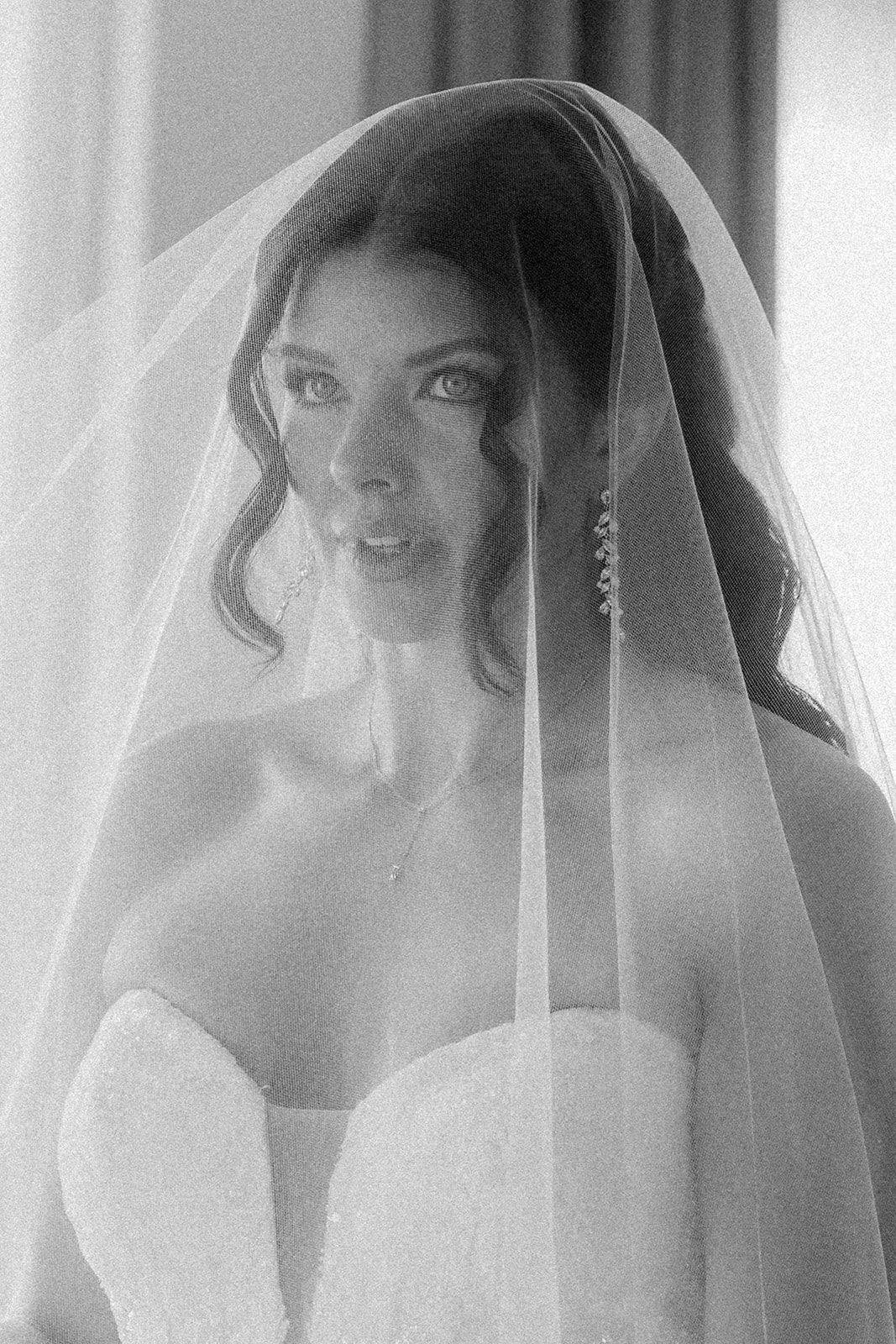 Black and white portrait of a bride wearing a strapless wedding gown and sheer veil, gazing softly at the camera.