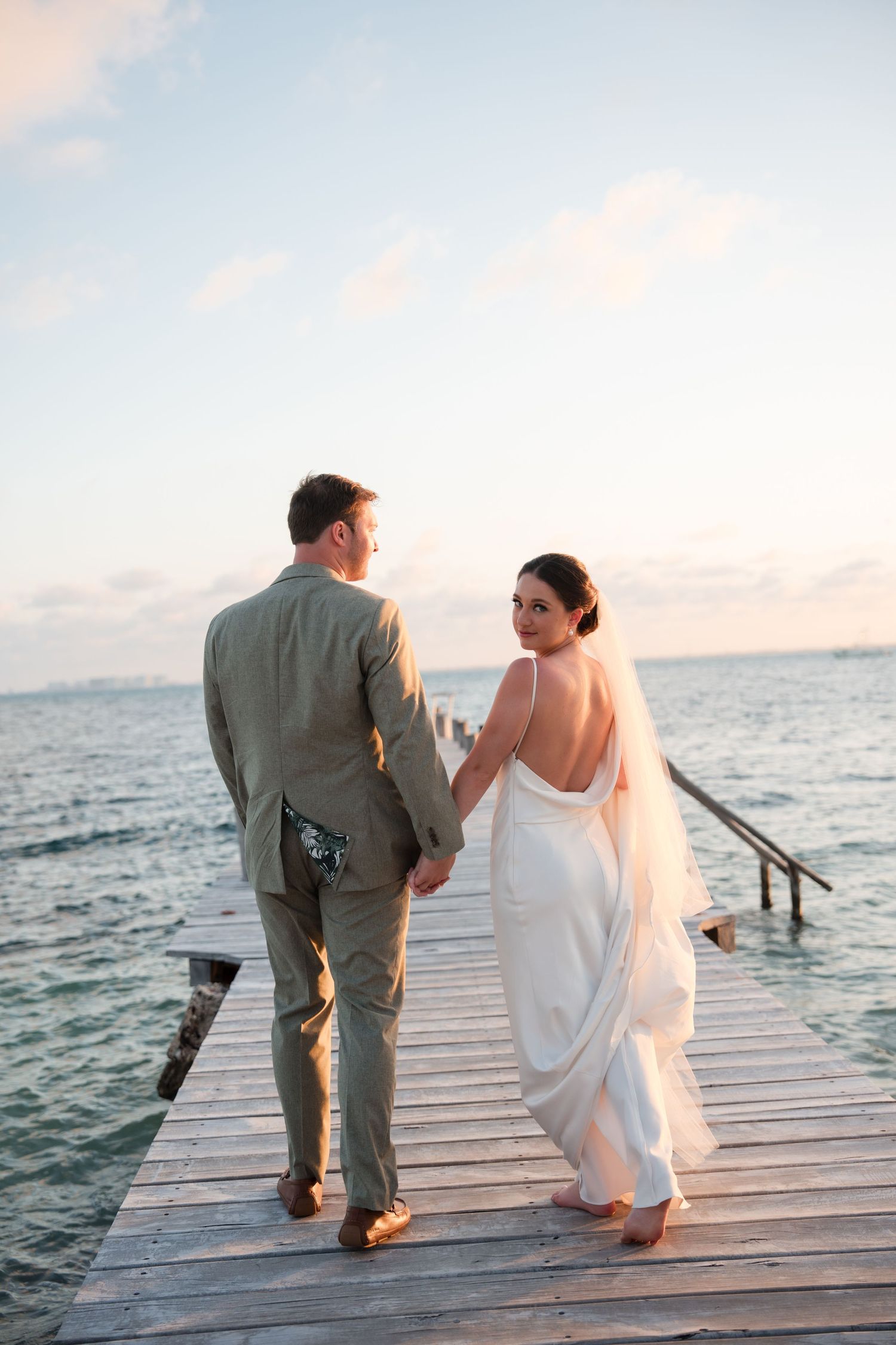 Bride looking back while walking with groom on a dock in isla Mujeres, Mexico