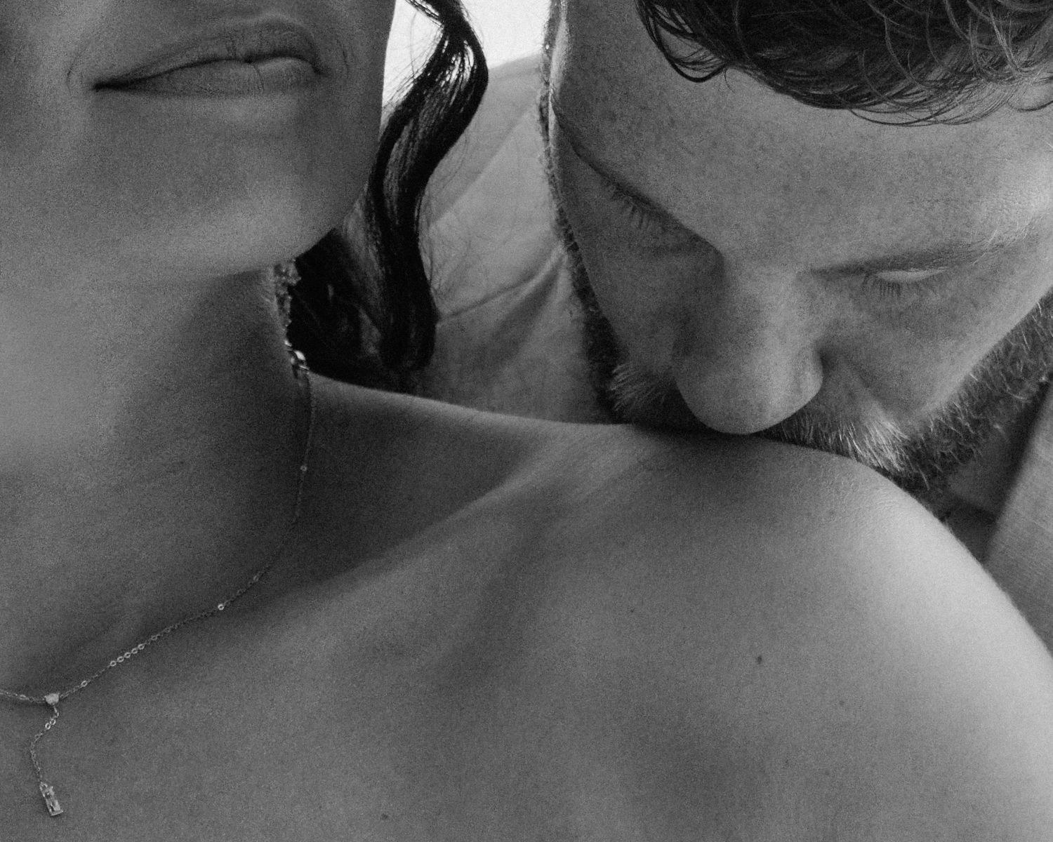 Black and white intimate photo of a groom kissing his bride's shoulder