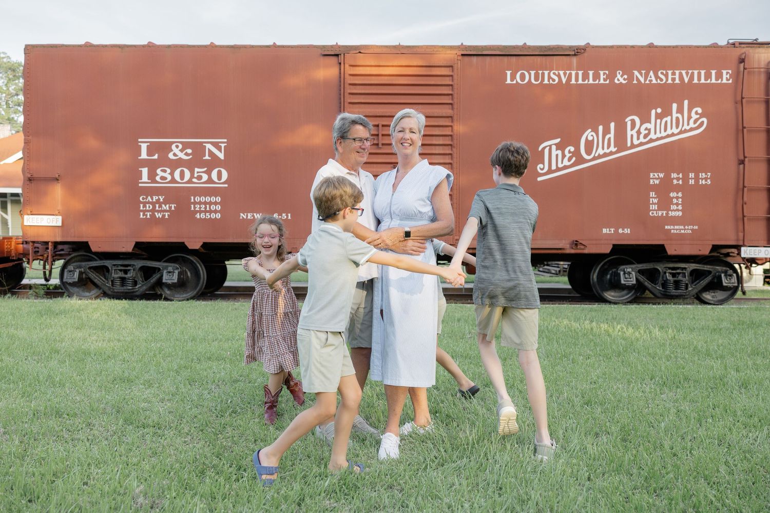 Family of five playing outdoors near a vintage Louisville & Nashville railroad boxcar labeled The Old Reliable.