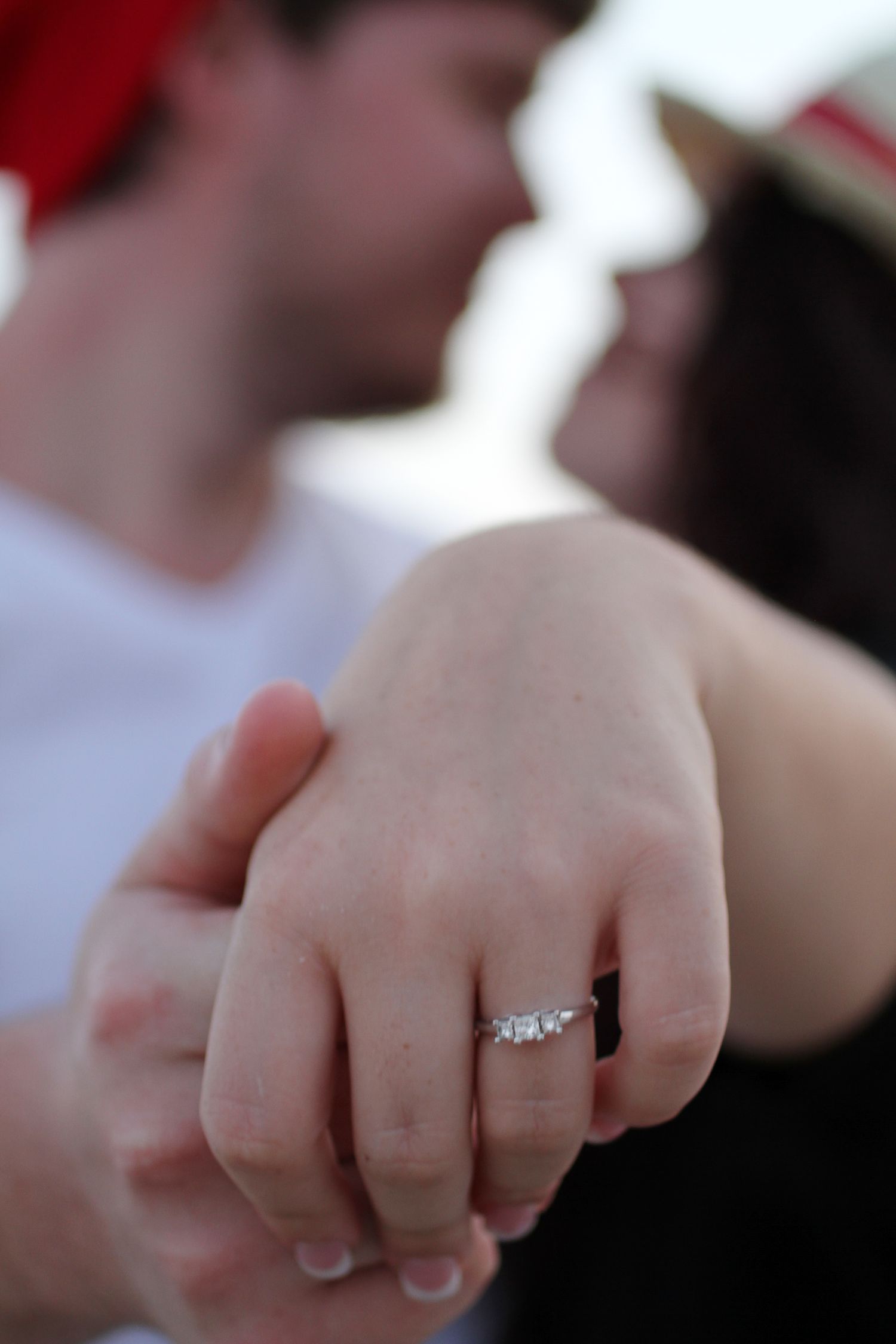 Close-up view of a hand with a diamond engagement ring on the ring finger against a blurred background.