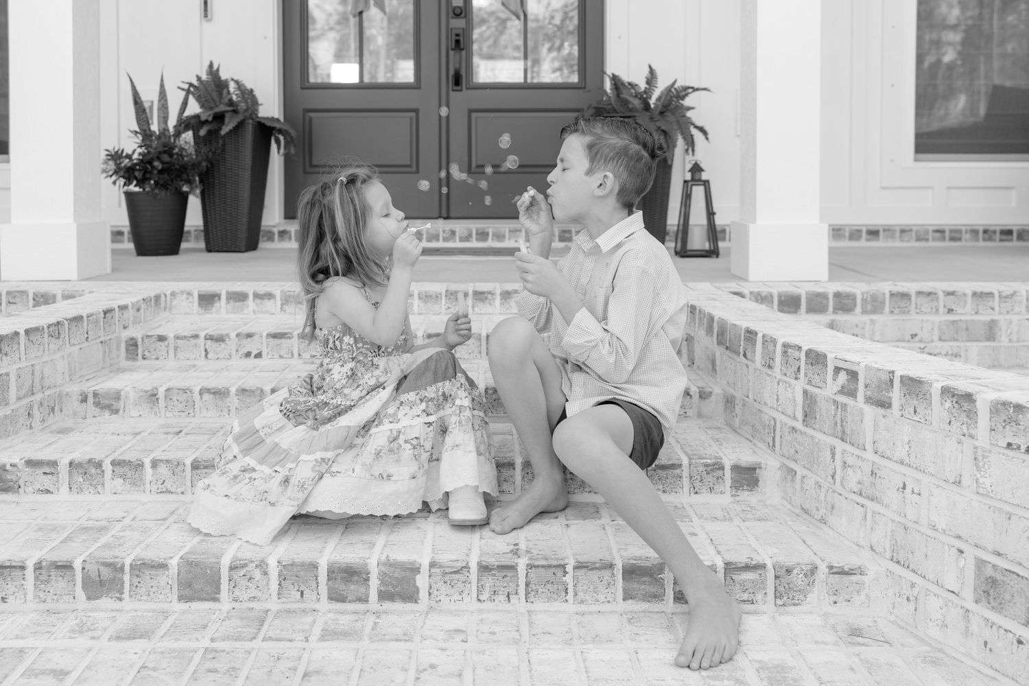 Two children sit on brick porch steps sharing a playful moment in black and white photography.