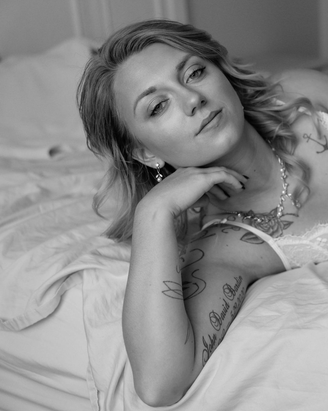 A black and white boudoir photo series showing a woman in white lounging on bedding with artistic poses.