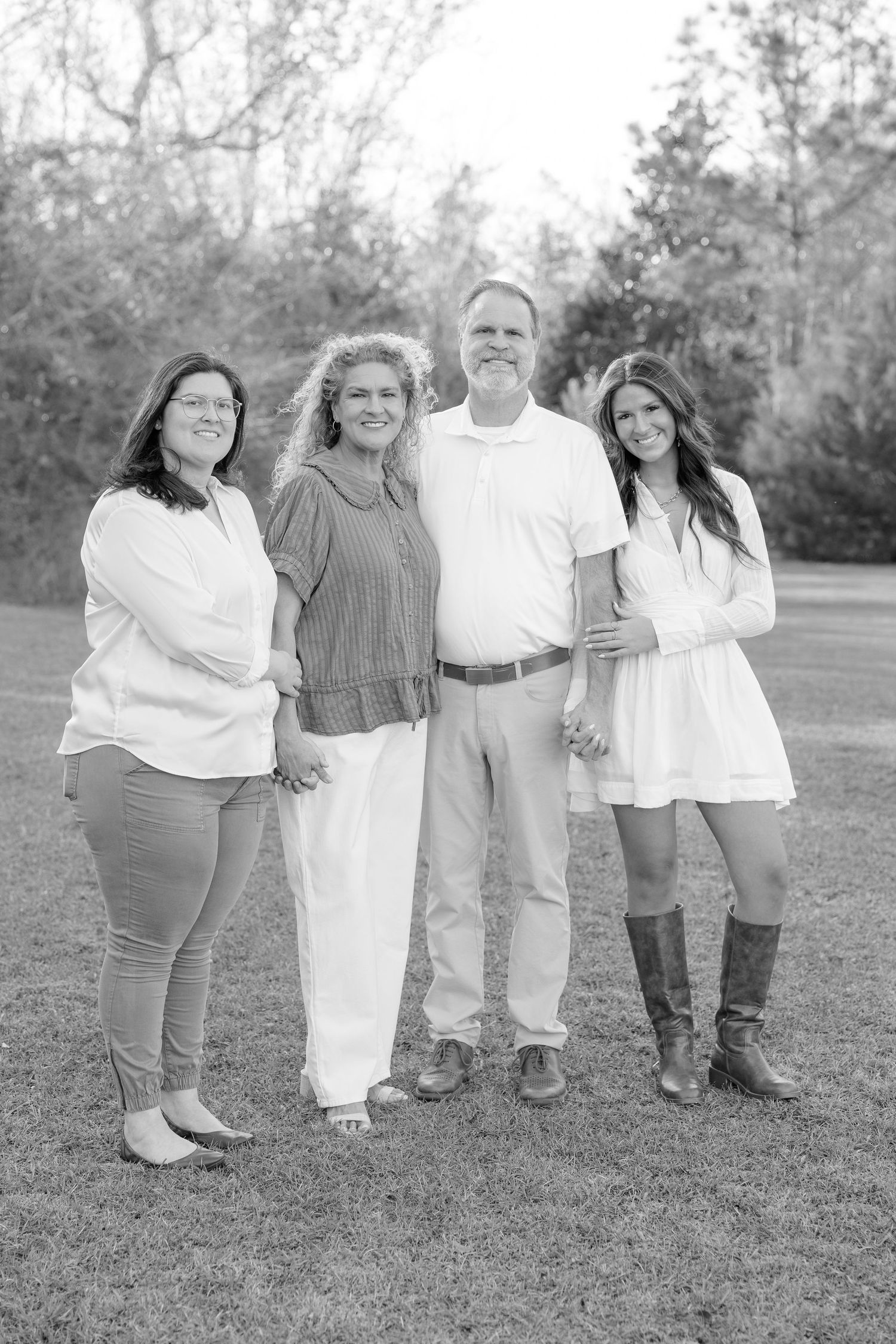 Black and white family portrait of four adults smiling outdoors on a grassy lawn with trees in the background.