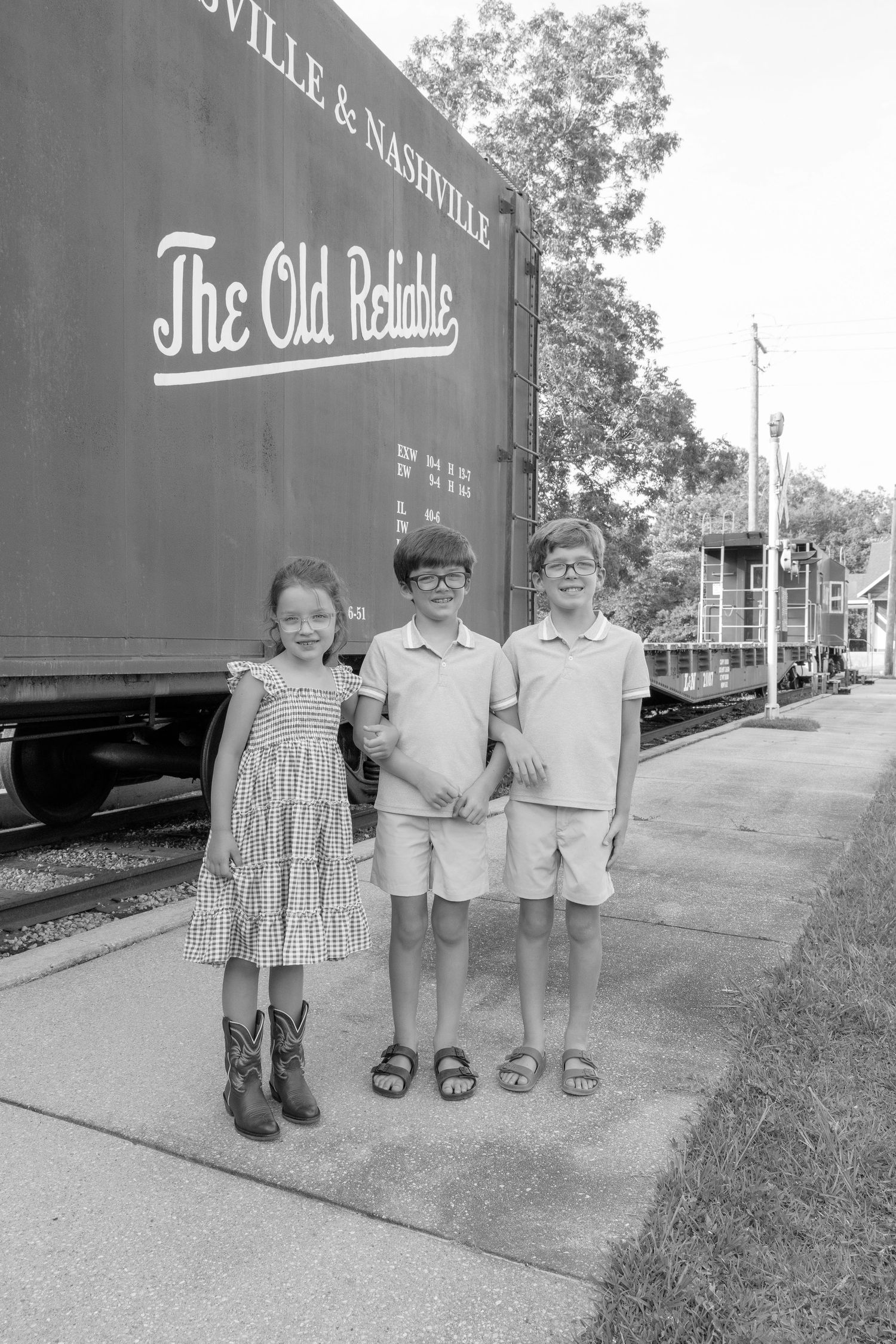 Three children pose in front of a Louisville & Nashville Railroad car labeled The Old Reliable in a black and white photo.