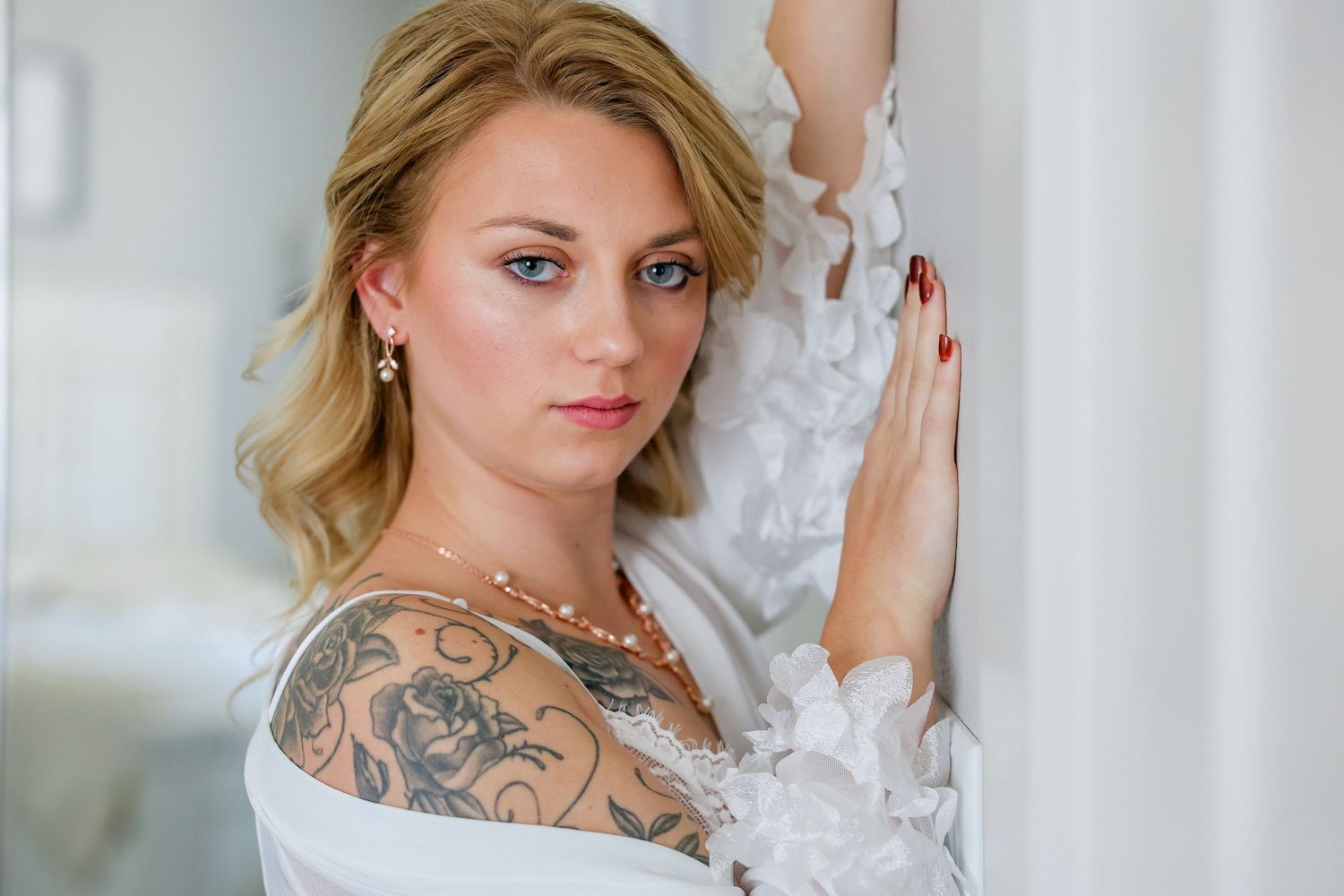 A woman in a white lace wedding dress poses elegantly against a light background.