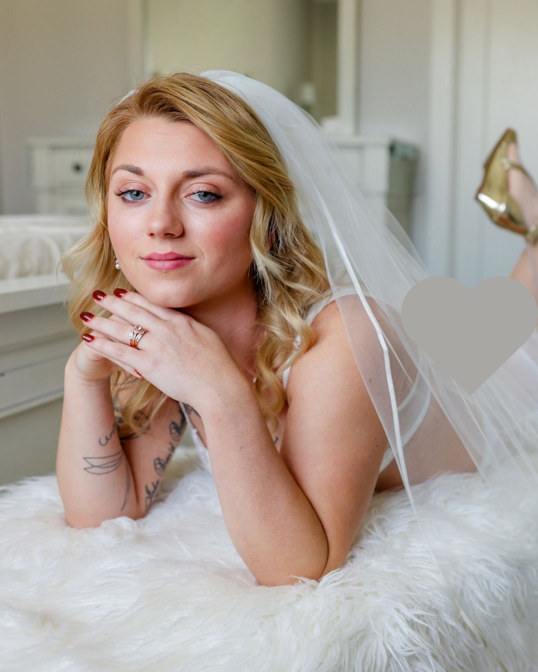 A person in a white dress lying on a plush surface in a romantic boudoir setting.