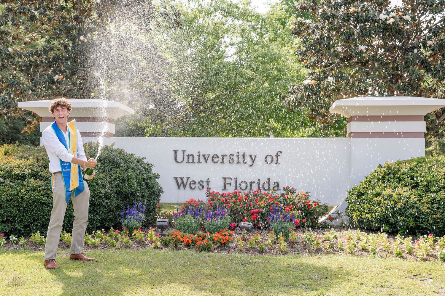 Graduate in cap and gown celebrating at University of West Florida sign with confetti popper.
