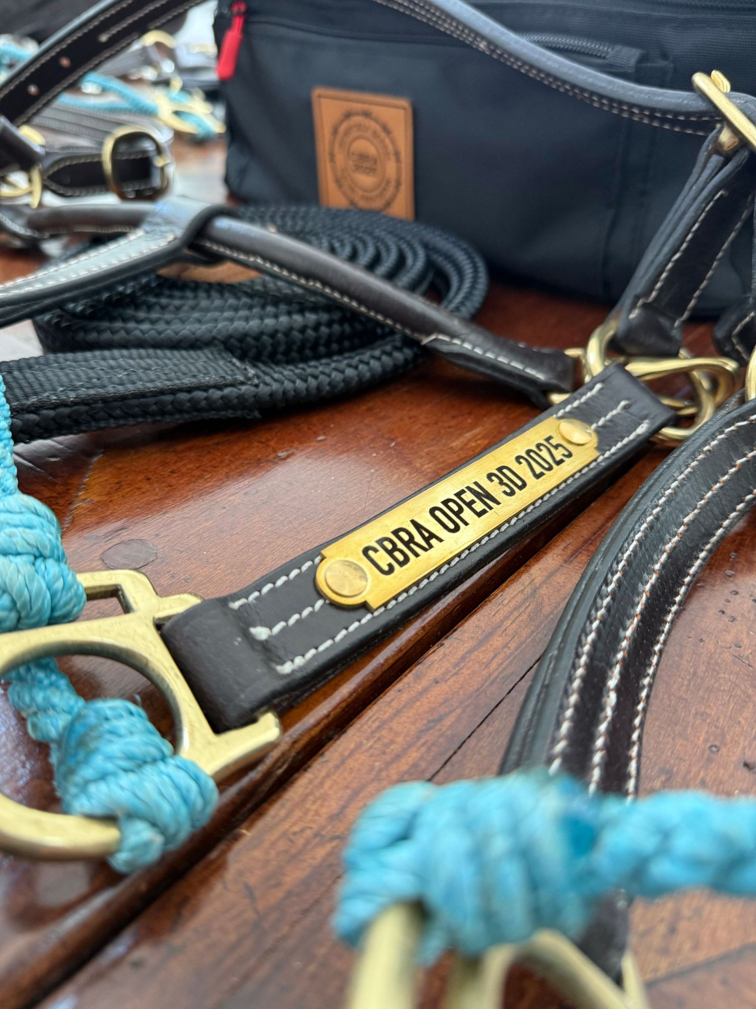 Close-up of black leather dog leashes with brass hardware and turquoise rope details on a wooden surface.