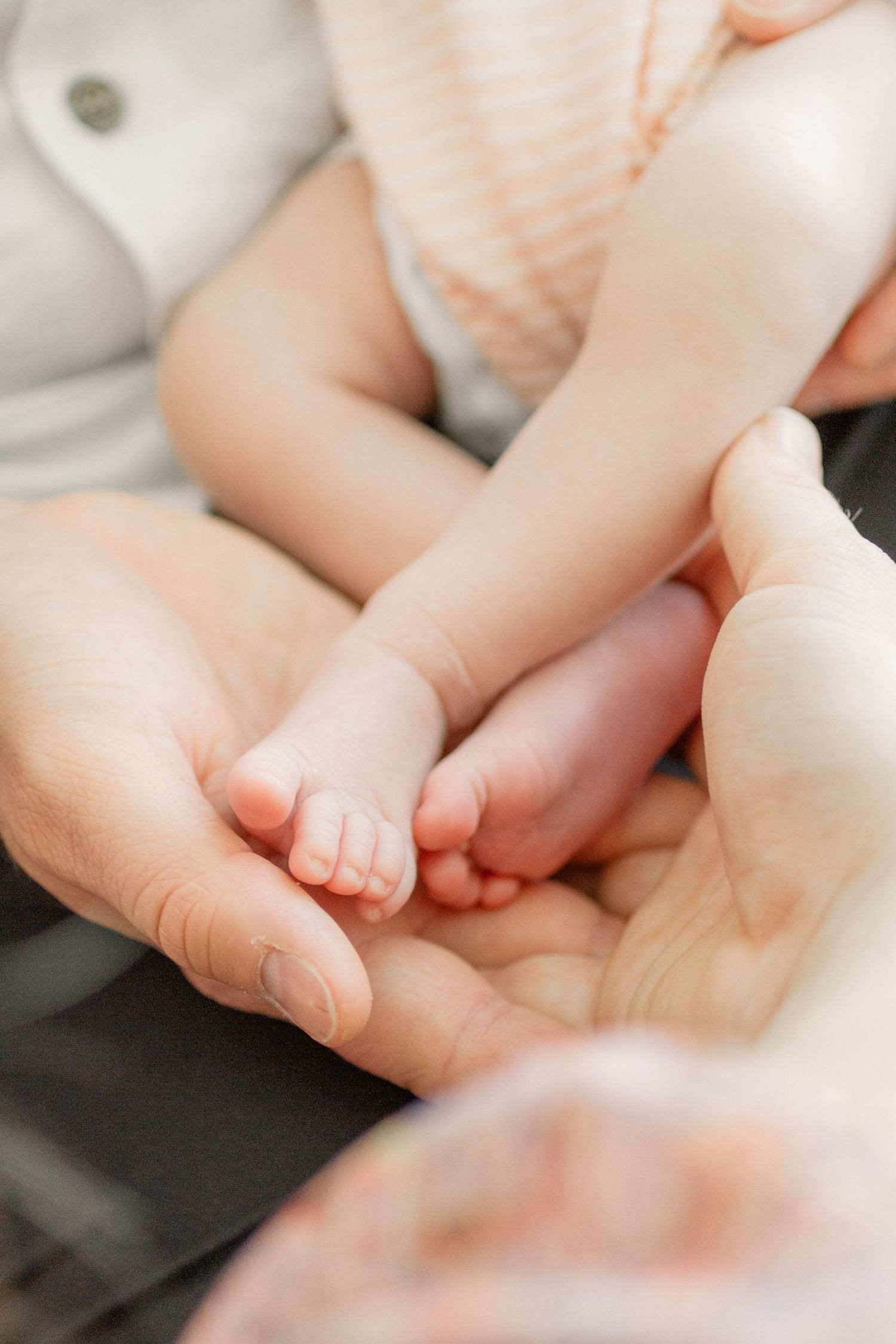 Close-up view of tiny baby feet being gently massaged by adult hands on a soft surface.