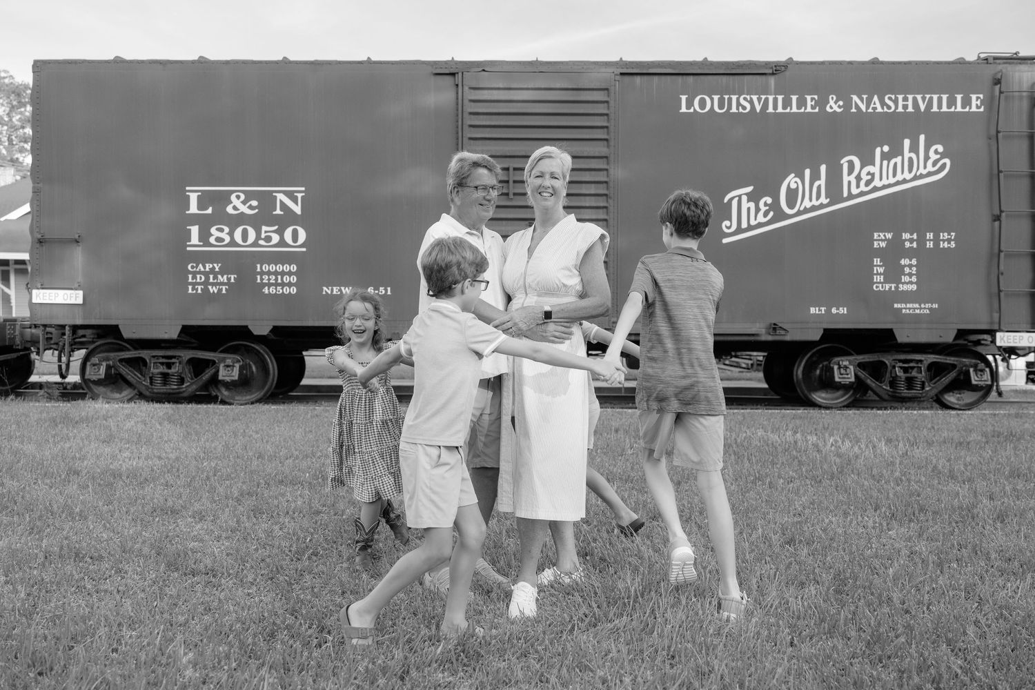 Black and white photo of a family posing in front of a Louisville & Nashville railroad boxcar on a grassy field.