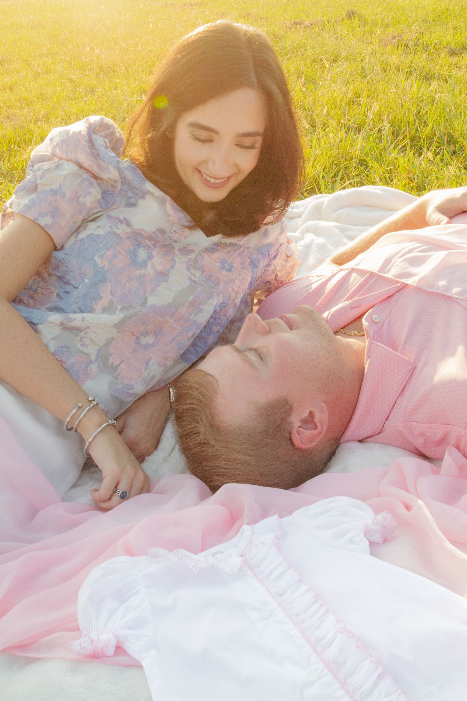 Romantic couple lying together on pink blanket in sunlit meadow with soft dreamy atmosphere.