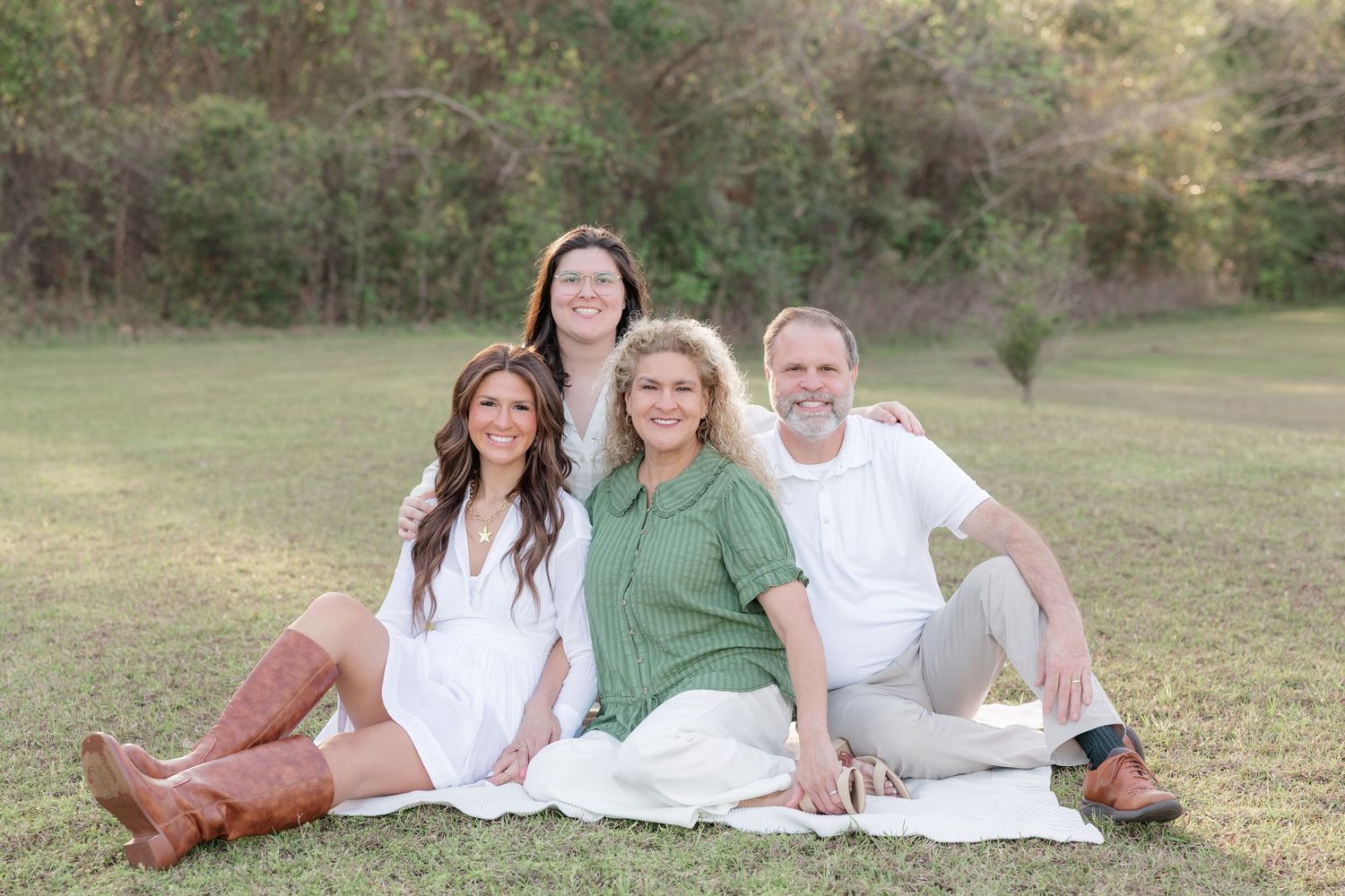 Family of four smiling together on a white blanket in a green field during a outdoor portrait session.