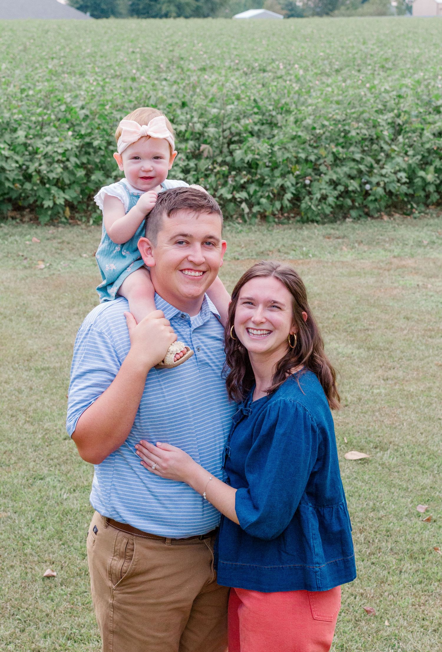 A couple shares a joyful moment together outdoors in a garden setting wearing blue and khaki clothing.