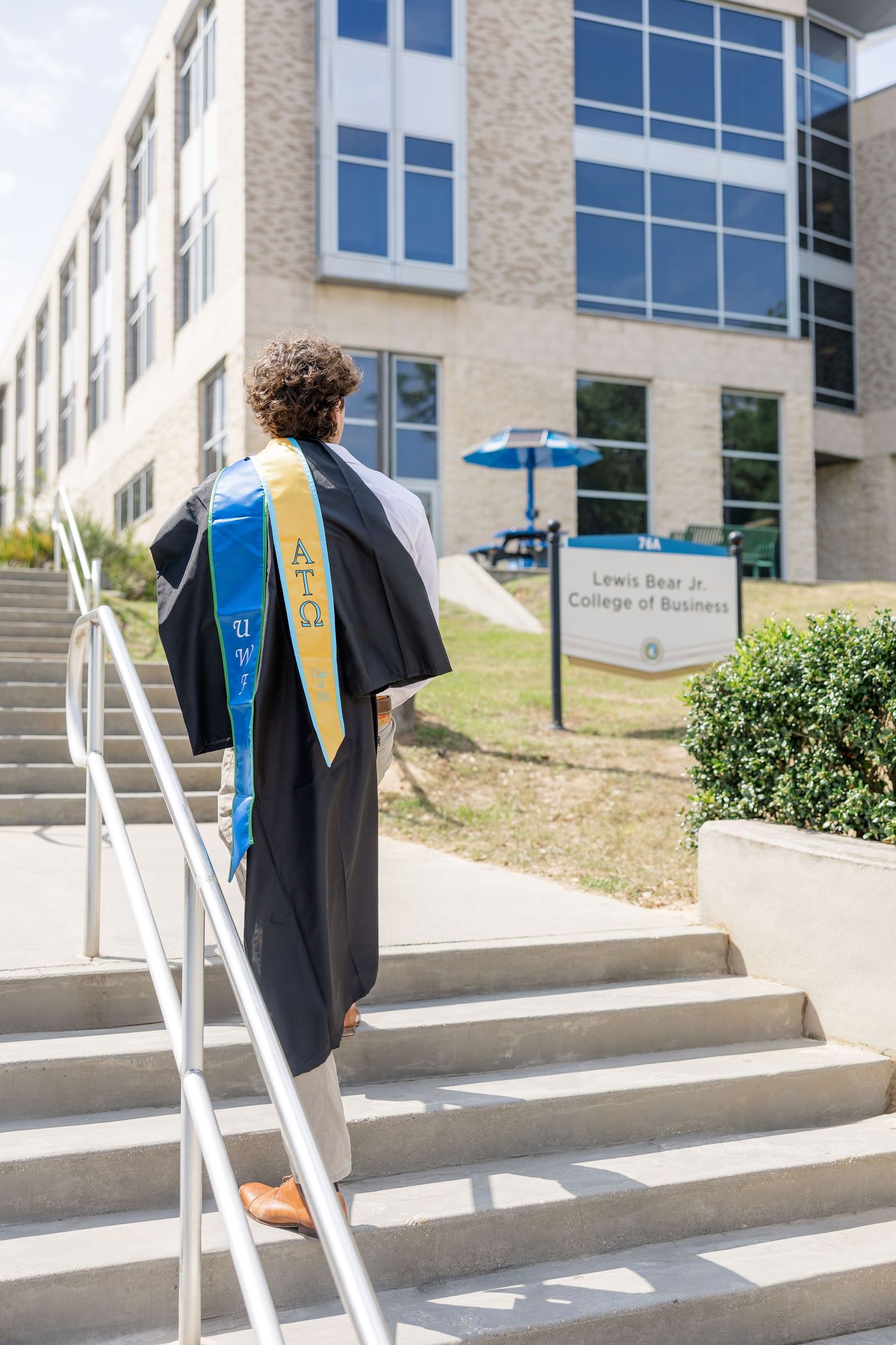 Graduate in black gown ascending steps toward Lewis Bear Jr. College of Business.
