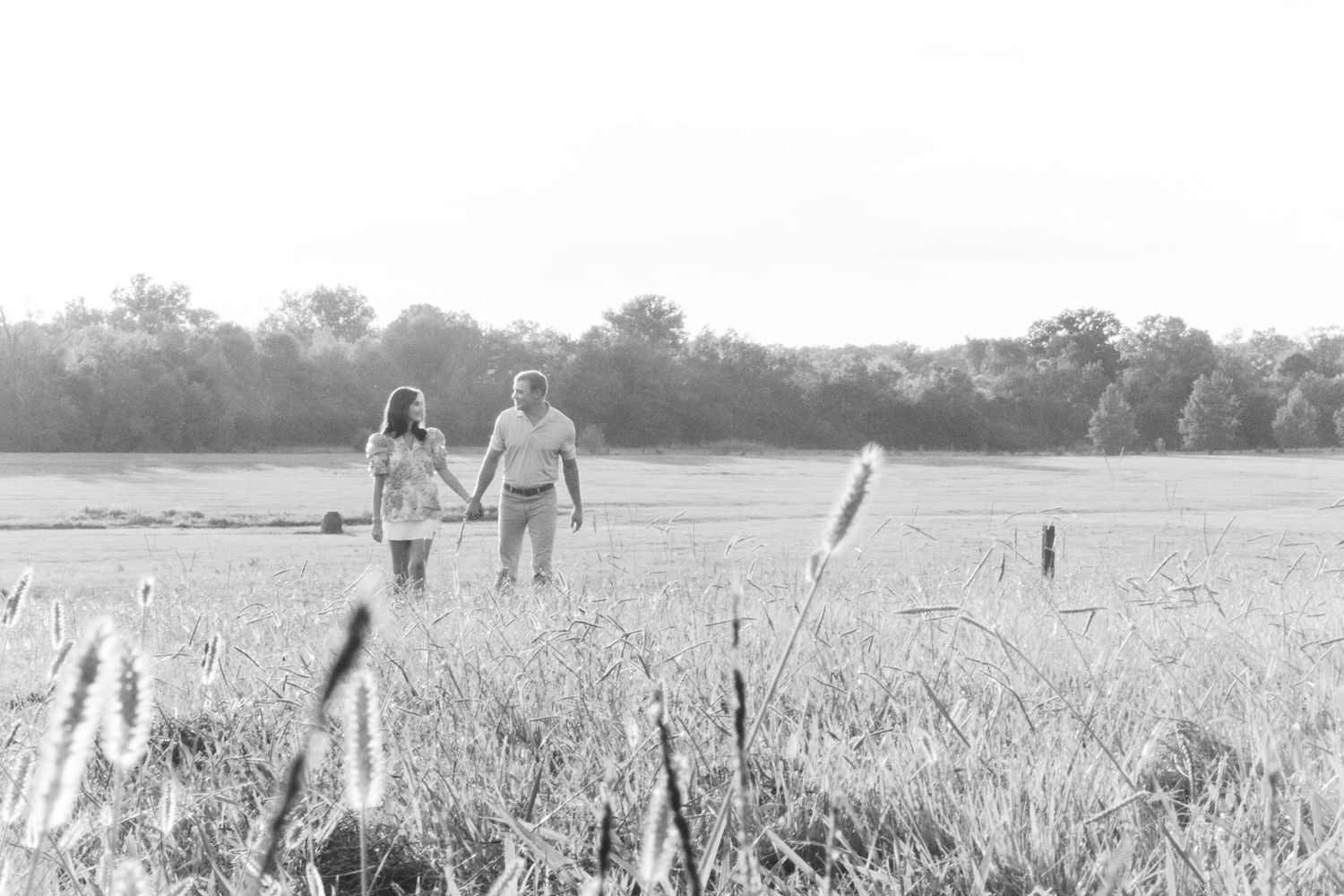 People walking through a tall wheat field on a summer day while holding hands.