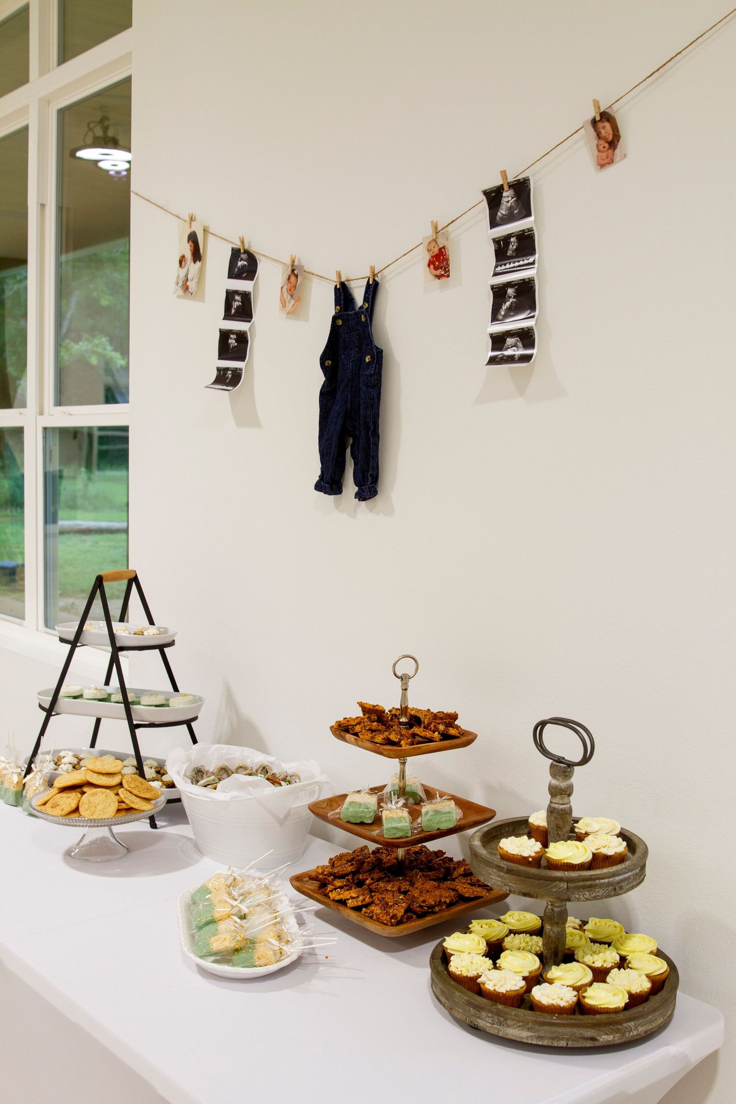 Appetizers and desserts arranged on tiered platters with baby clothes hanging on string above.
