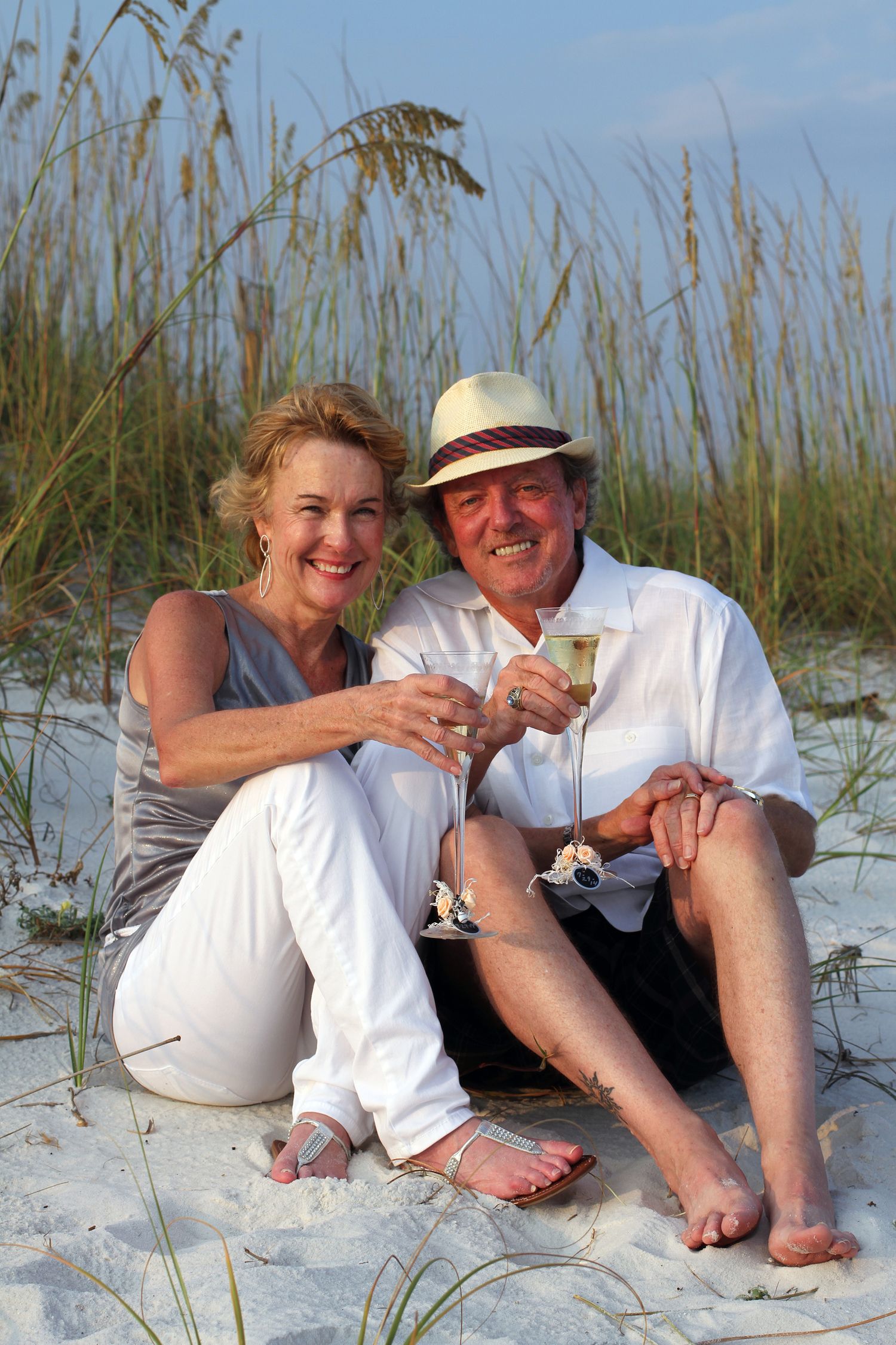A couple relaxing together on a white sandy beach with sea grass on a sunny day.
