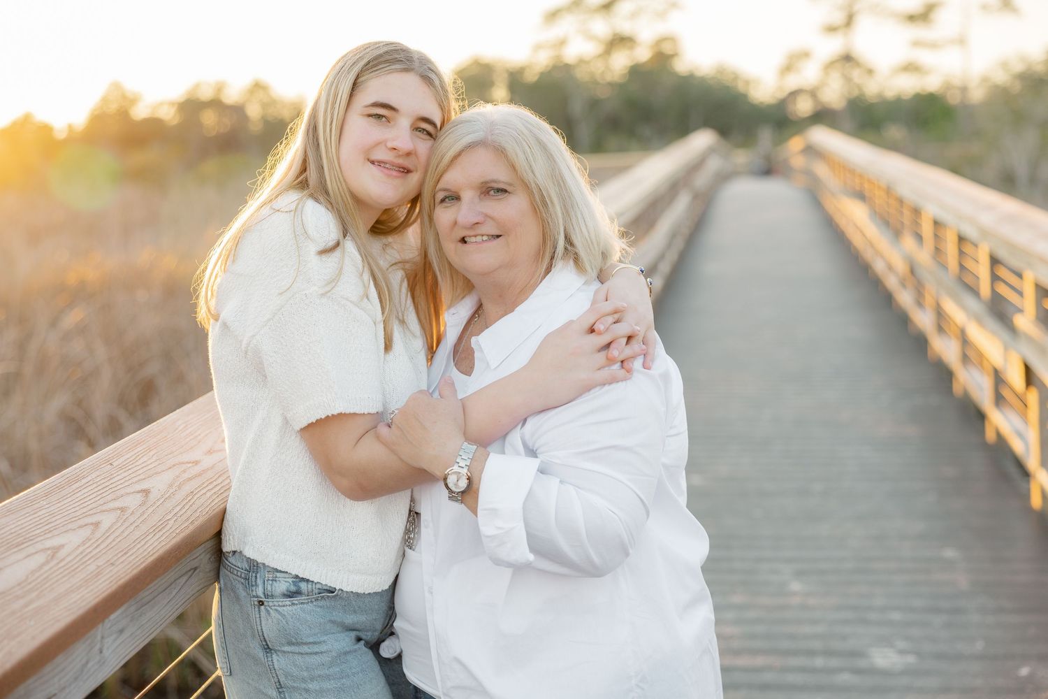 Two people share a joyful embrace while walking on a wooden boardwalk during golden hour.