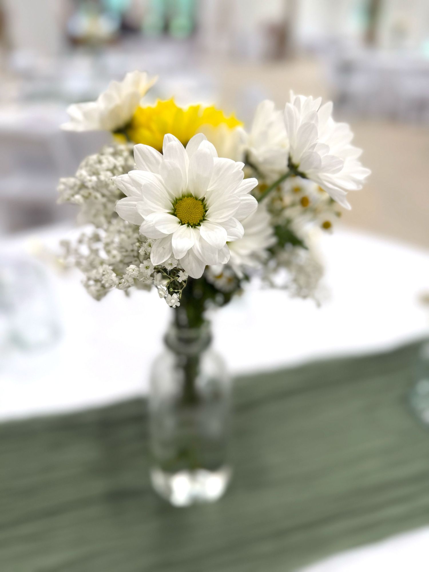 White daisies and baby's breath flowers arranged in small vases on a green table runner.