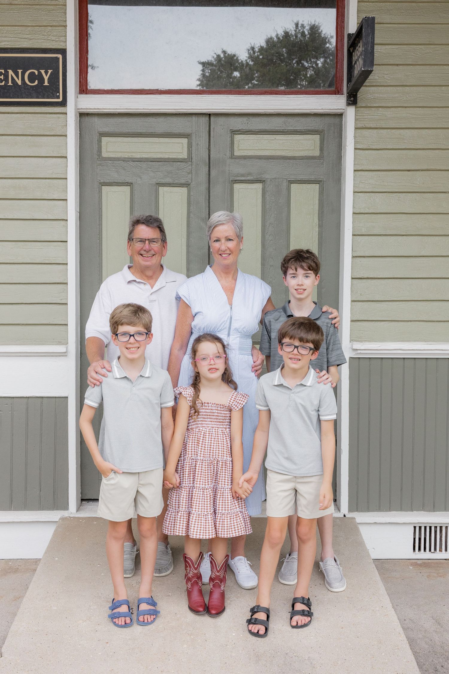 Family of six posing in front of green double doors, including parents and four children dressed in coordinating outfits.