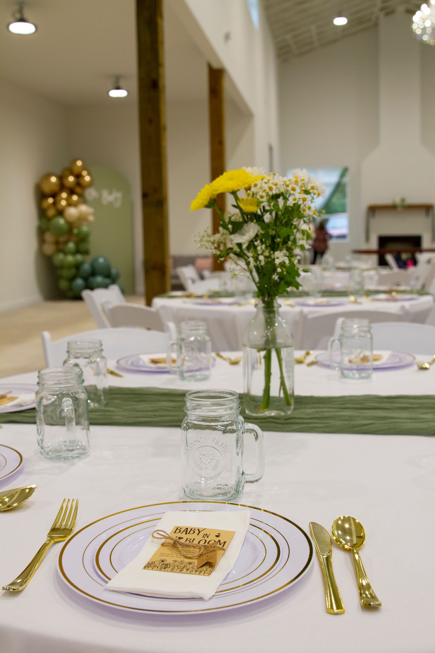 An elegant table setting with white plates, gold cutlery, mason jars and delicate floral centerpieces.