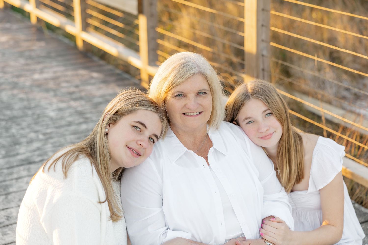 A family in white outfits poses together outdoors on wooden steps for a professional photo session.