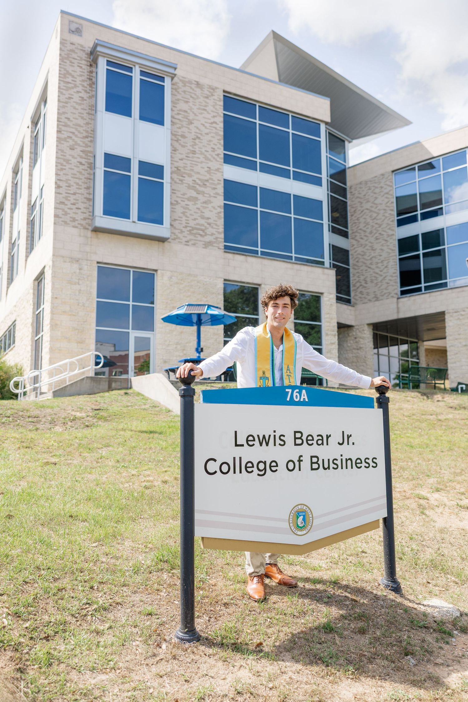 Graduate poses proudly in front of Lewis Bear Jr. College of Business sign wearing graduation sash and medals.