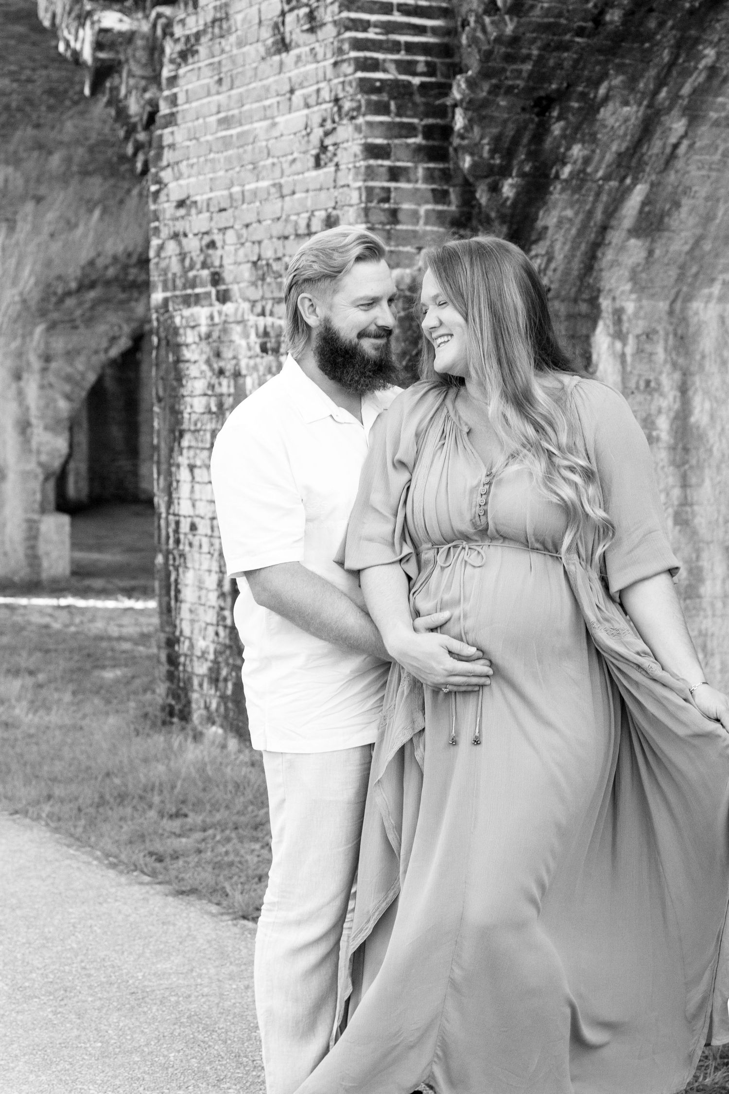 A romantic couple embraces outdoors near an old brick wall in a series of intimate black and white photographs.