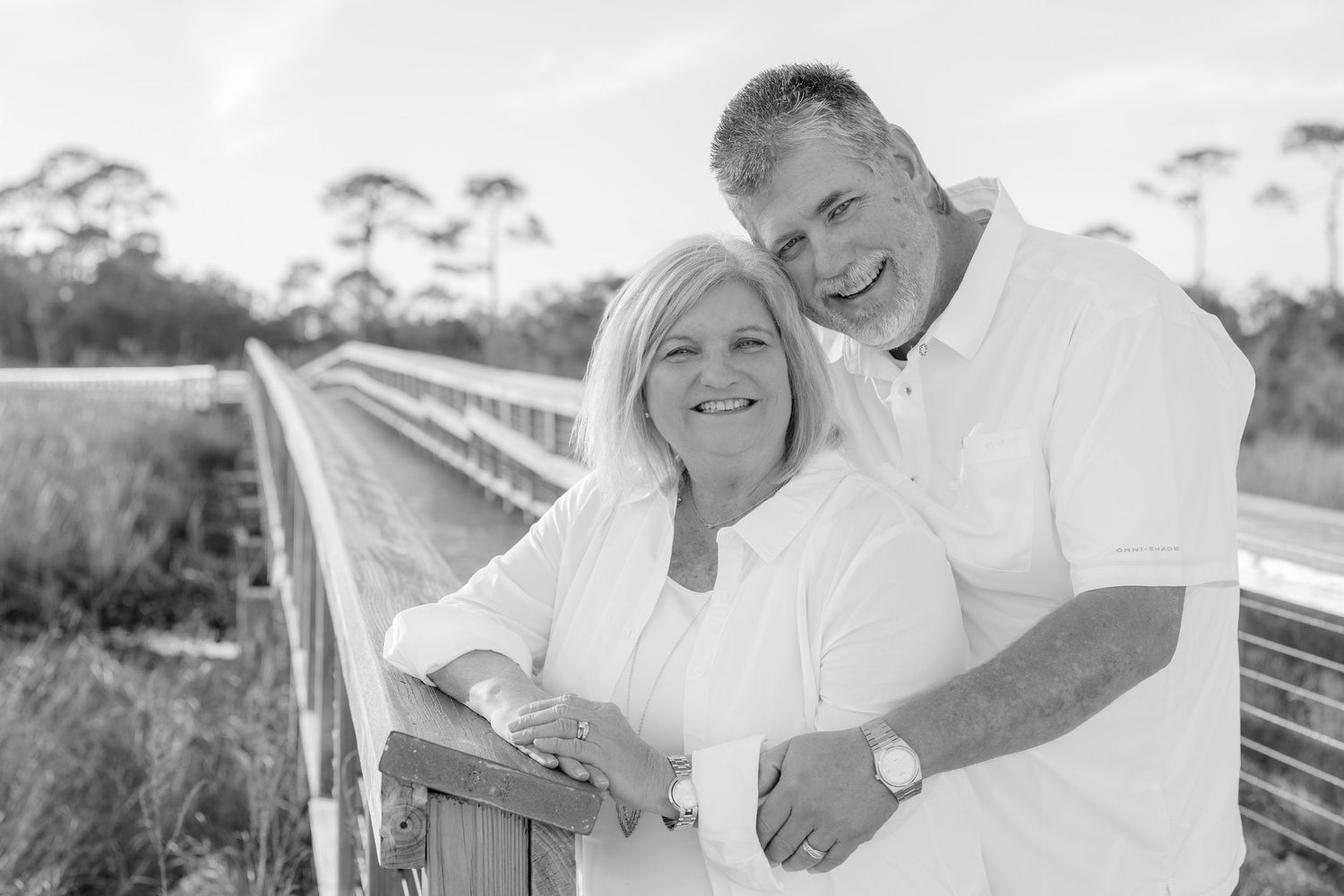 A happy couple in white clothing poses for a collage of romantic outdoor photos on a beach boardwalk.