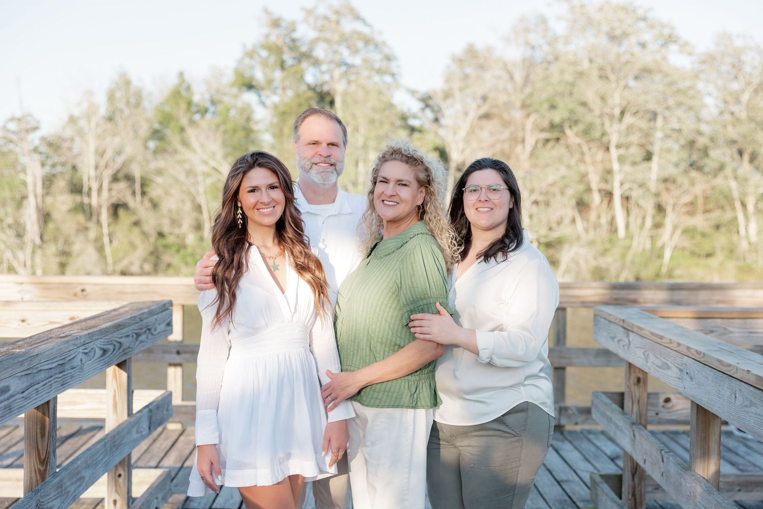 Family of four posing together on a wooden bridge during an outdoor portrait session in natural light.