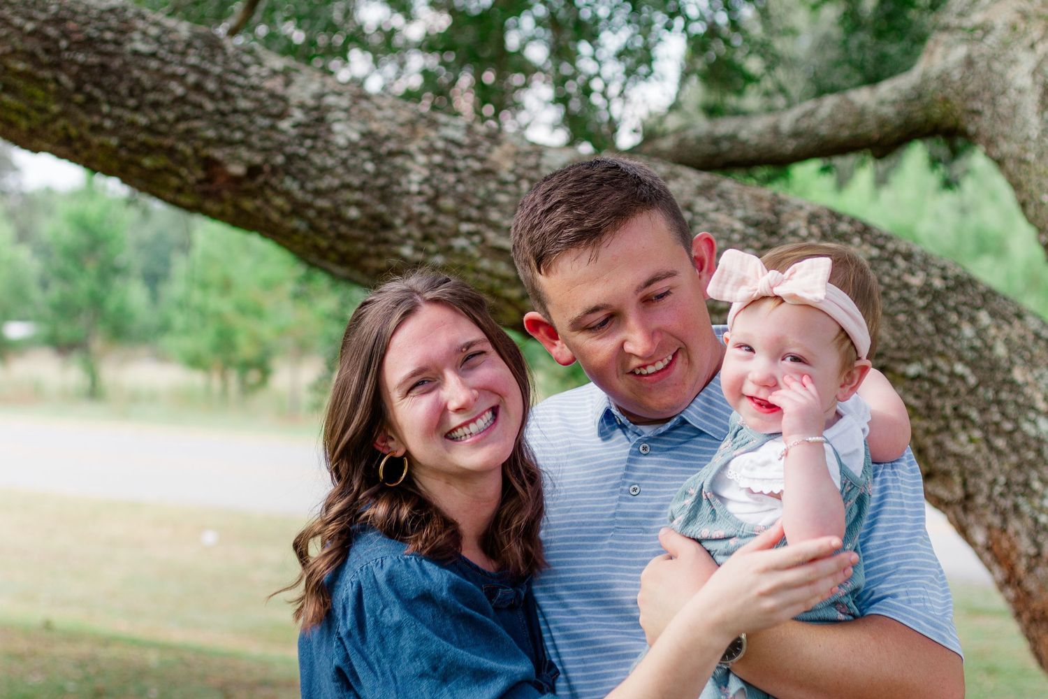 A happy family shares a joyful moment together under a large tree branch in an outdoor setting.