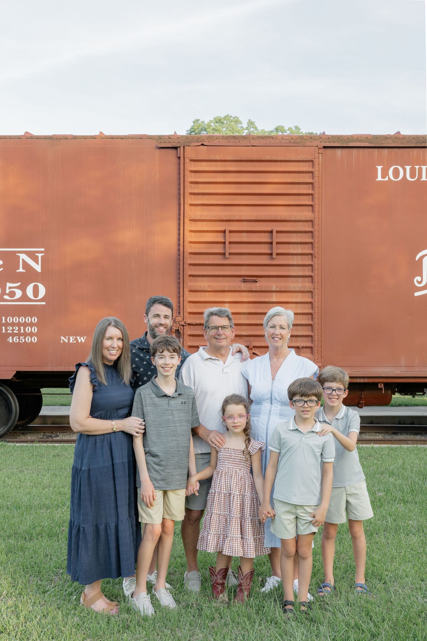 Multi-generational family of seven posing together in front of a rustic red Louisville & Nashville train boxcar.