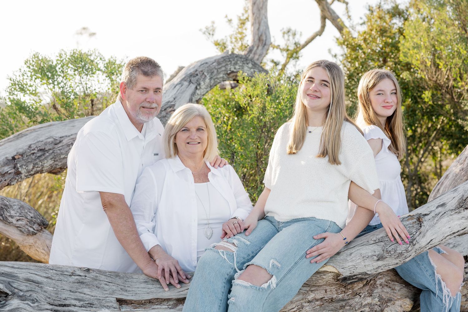 A group wearing coordinated white and denim outfits poses together outdoors in a natural setting during golden hour.