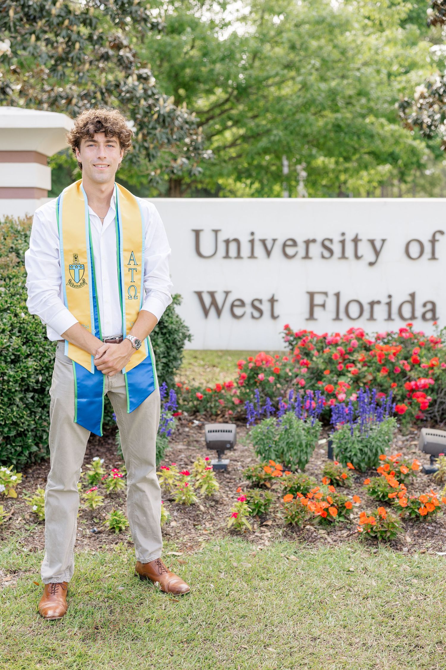 Male graduate in gold stole standing before University of West Florida campus sign.