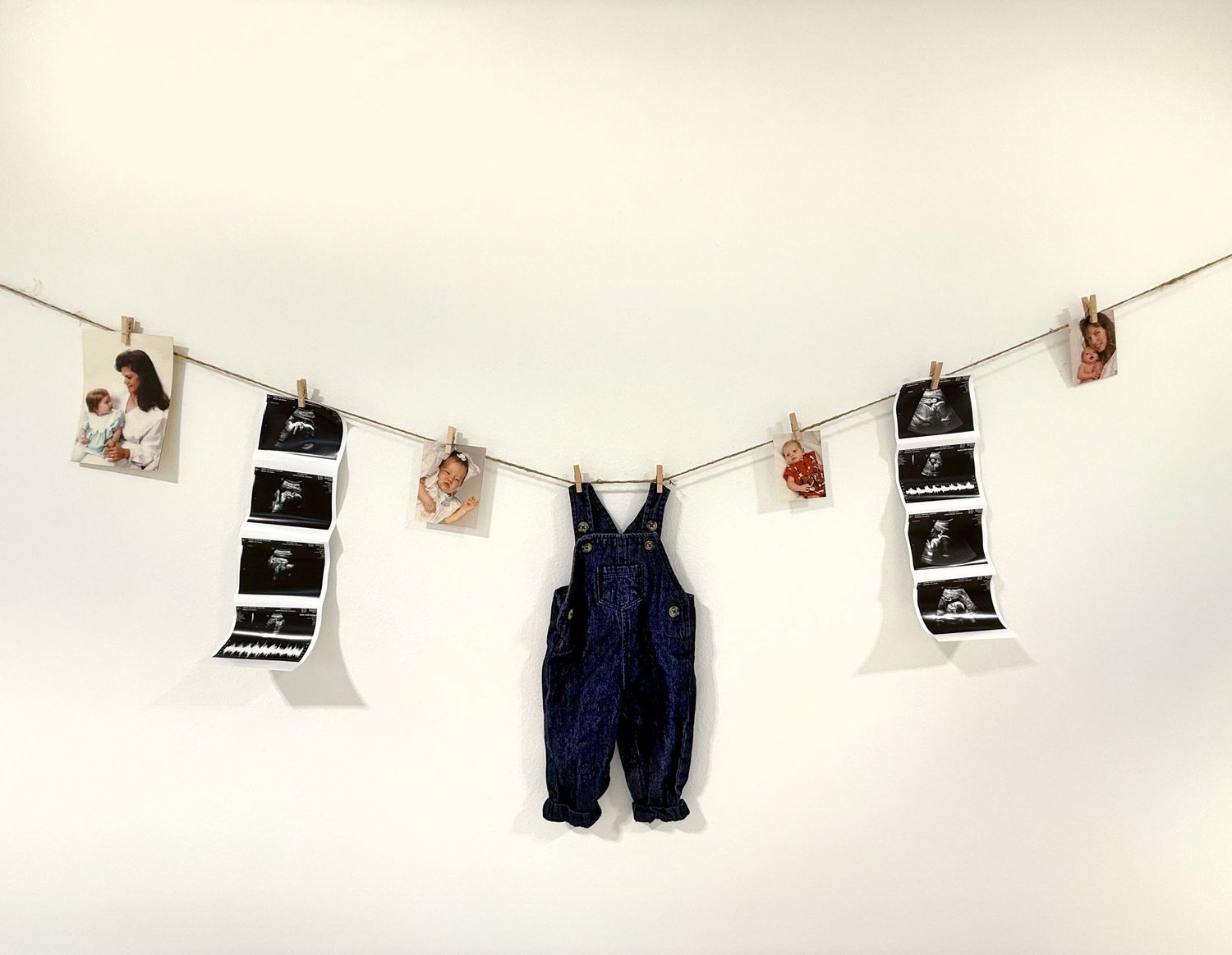 A clothesline display of black and white photographs with tiny denim overalls hung between them.