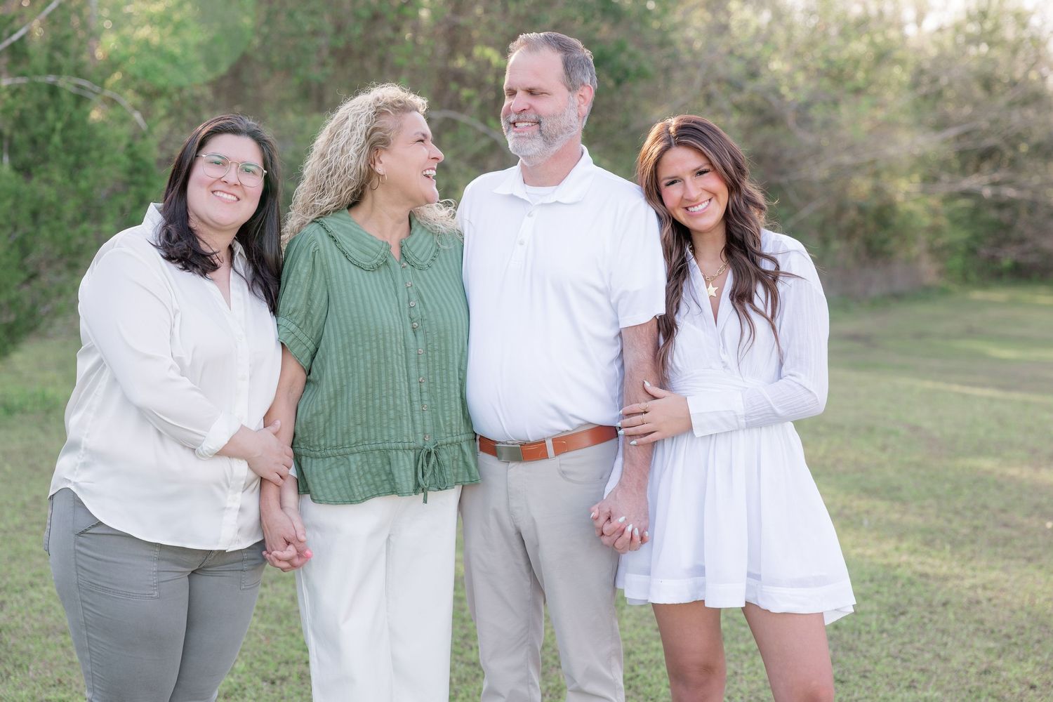 Family of four smiling together outdoors on green grass during a professional portrait session.