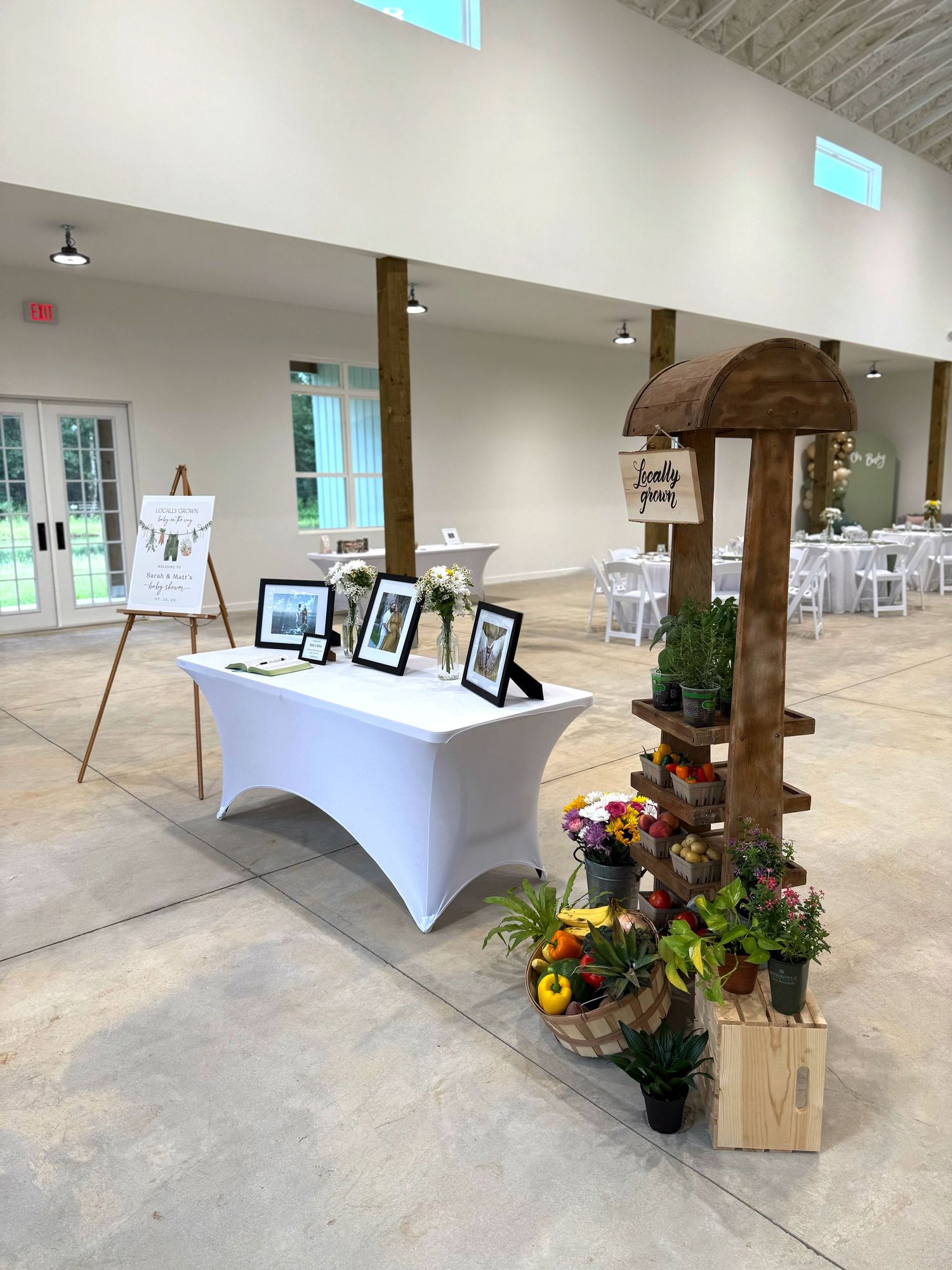 Gallery space displays white tables with decorative floral arrangements and rustic wooden accents along a concrete floor.