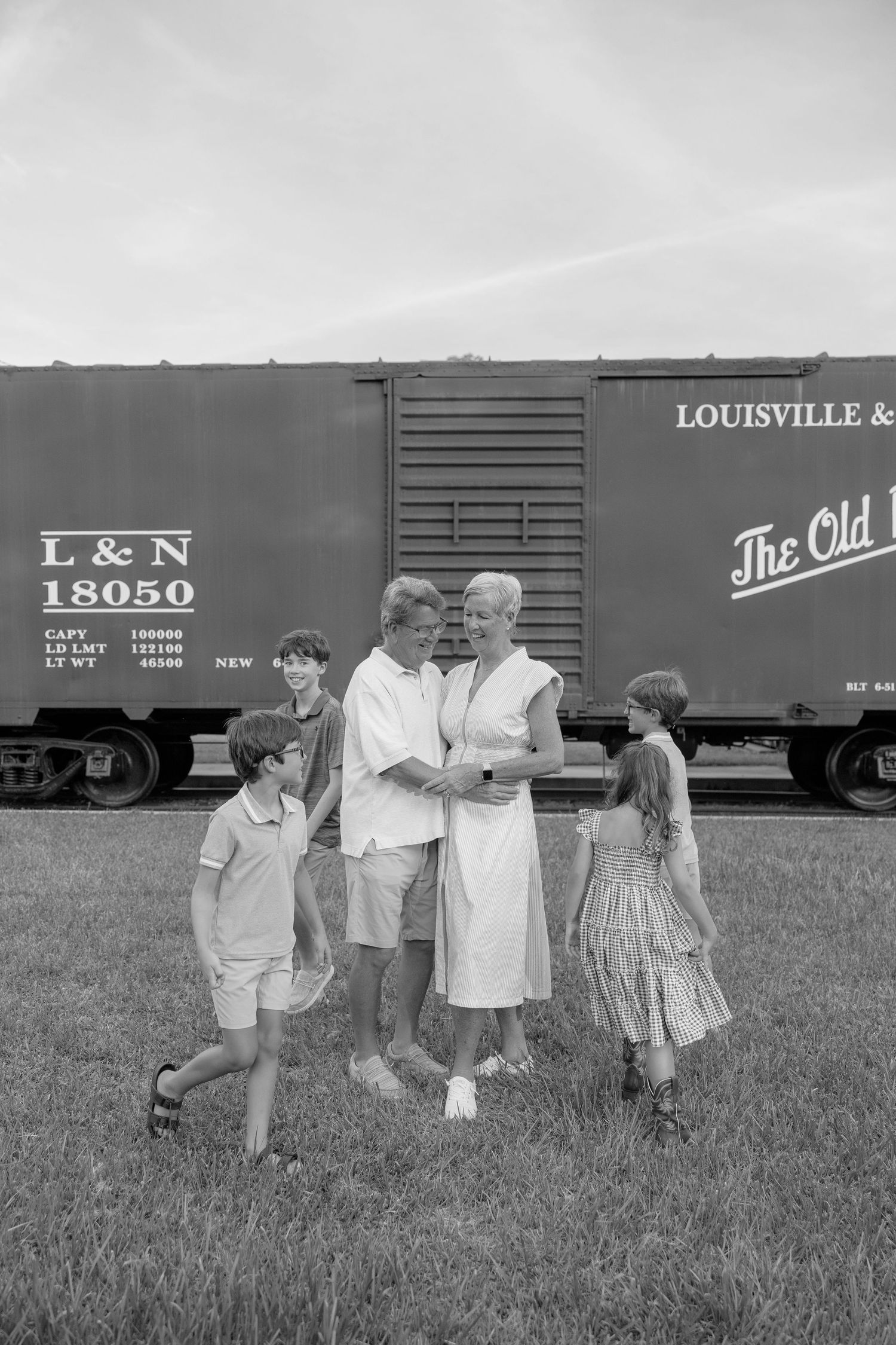 Black and white photo of a family gathering near a Louisville & Nashville railroad boxcar on a grassy field.