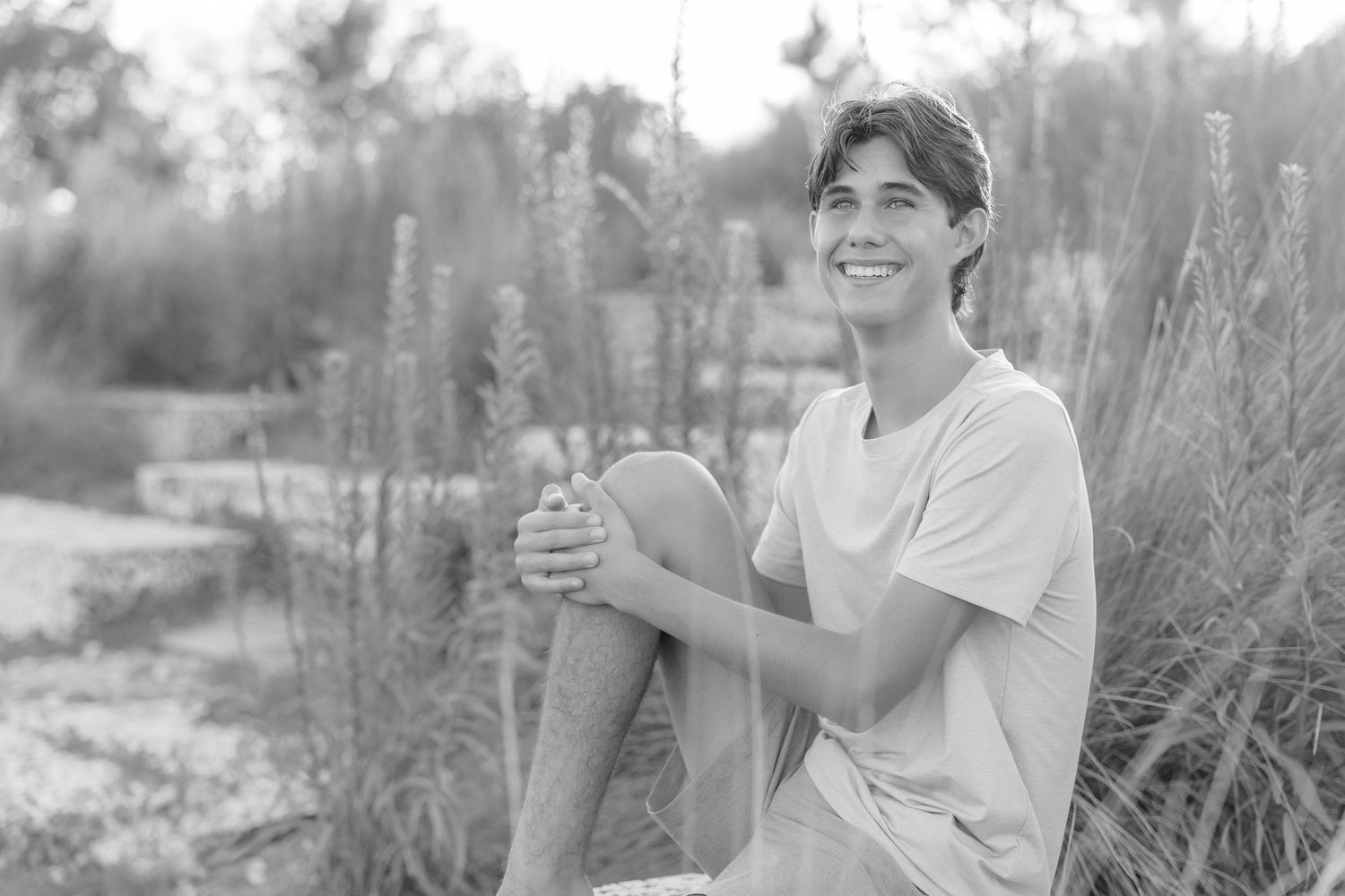 Smiling young man sitting outdoors in a field, black and white portrait photo.