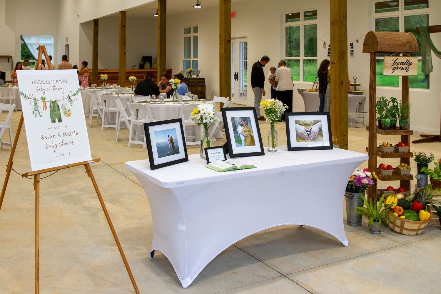 A baby shower dessert table setup with various treats, white tablecloths, and framed photos on display.