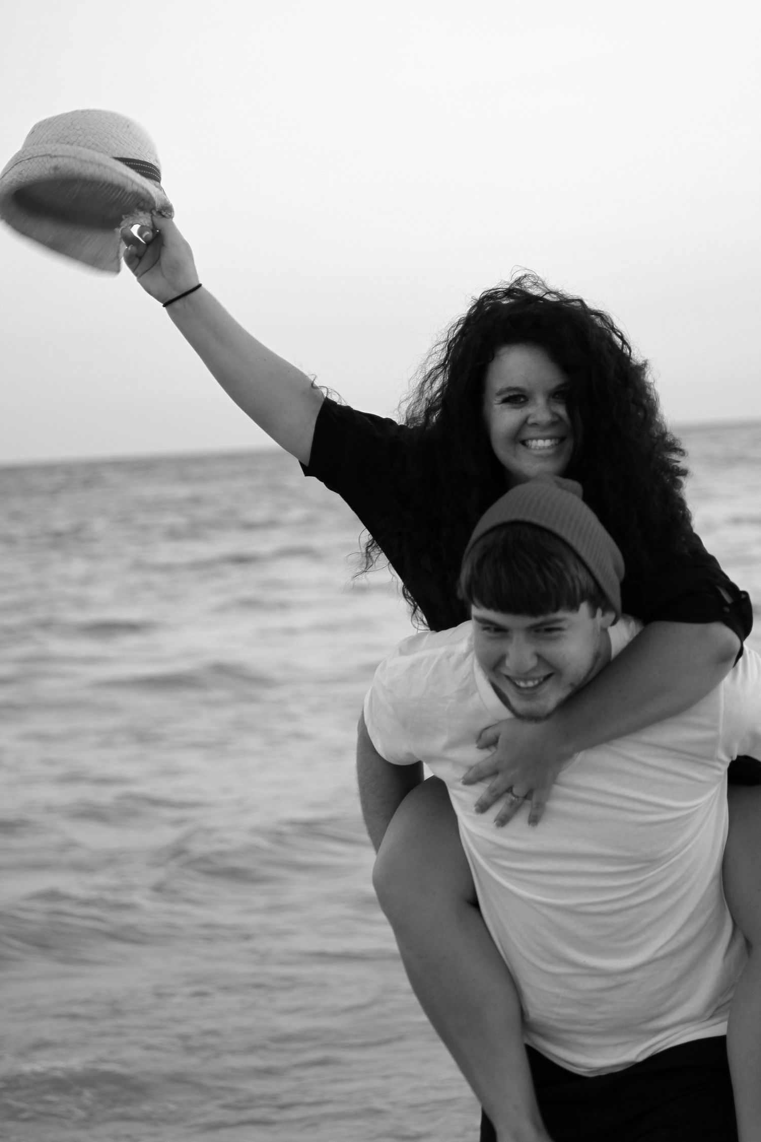 Four candid black and white photos show joyful moments of friendship at the beach with people embracing and laughing together.